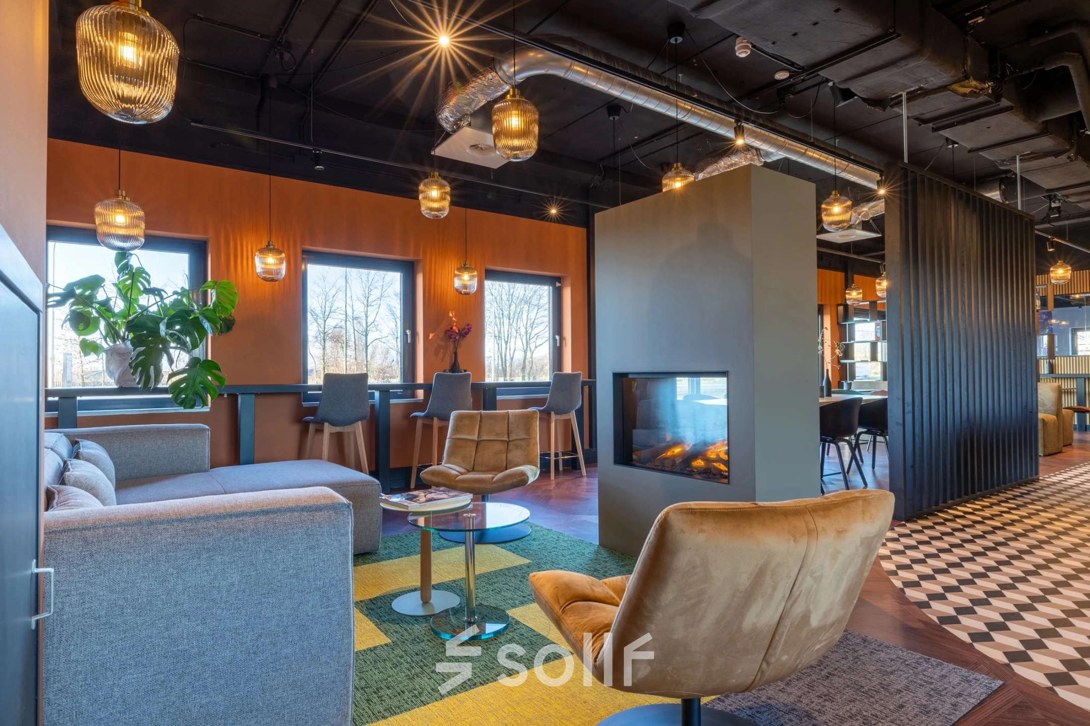 Furnished office space in Gouda at Zuidelijk Halfrond 1 with modern seating arrangements around a central fireplace, multiple tables, and ambient lighting. Ideal for office space rental.