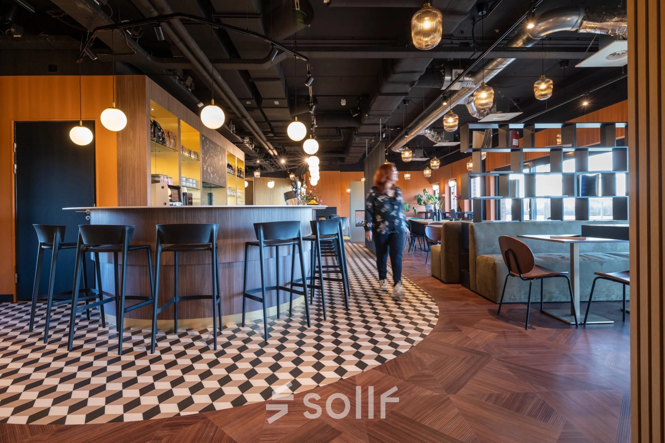 Modern office space in Gouda featuring a stylish bar area with seating, highlighting available office space rental at Zuidelijk Halfrond 1. A person is walking through the bright, welcoming environment.