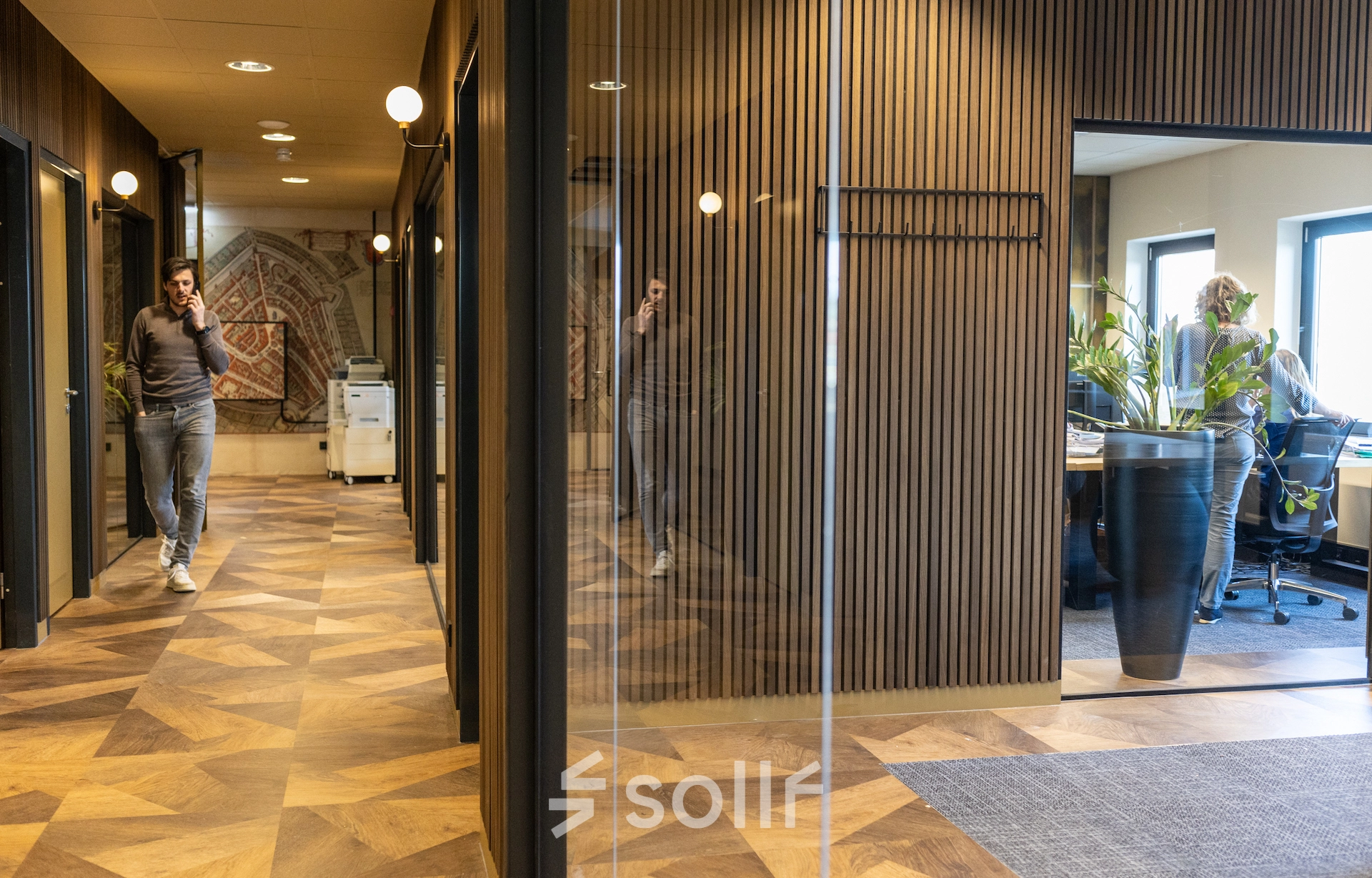 Modern office space at Zuidelijk Halfrond 1, Gouda, featuring wooden flooring, glass walls, and a well-lit interior with people engaged in business activities. Ideal for office space rental.