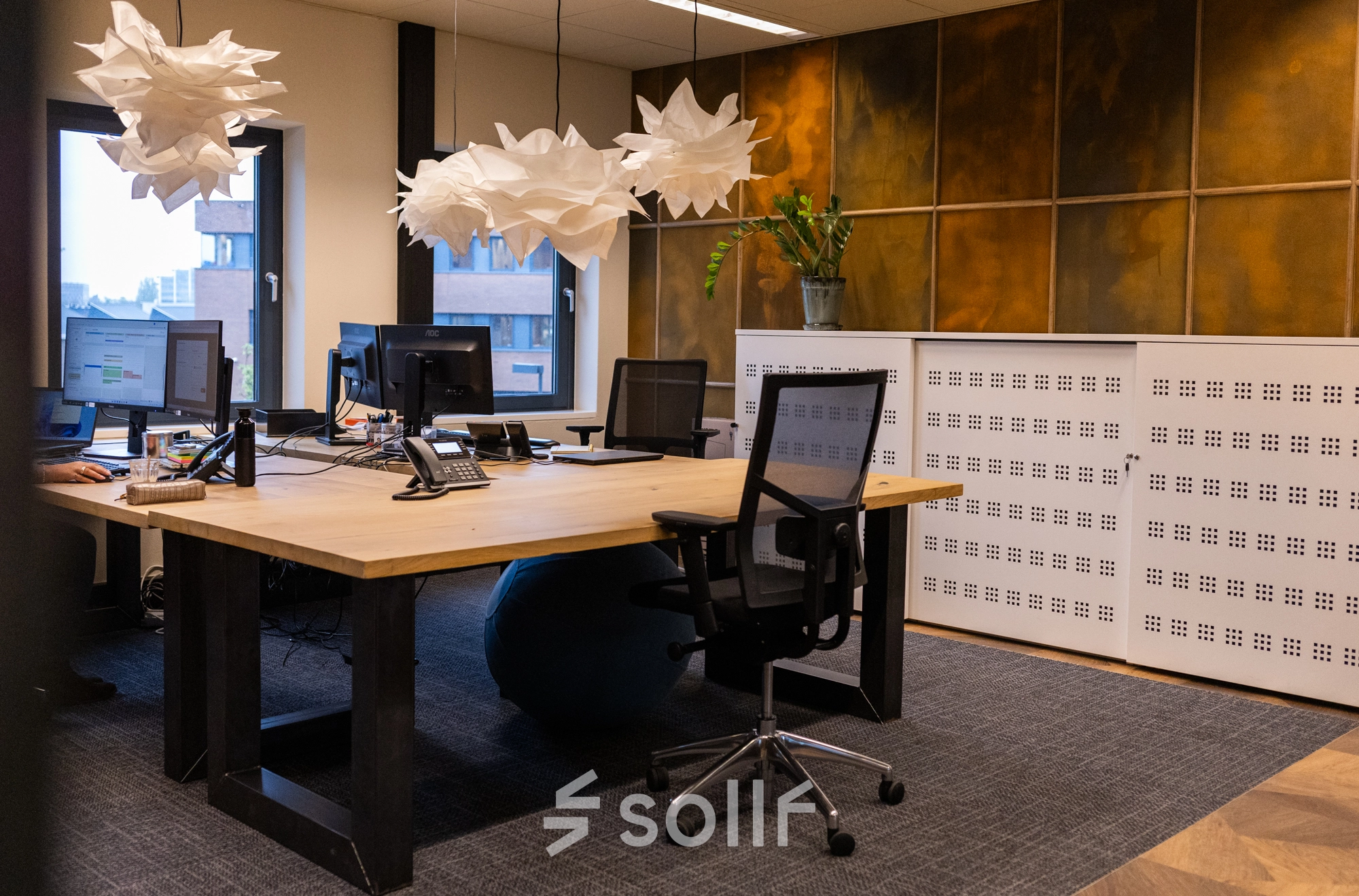 Modern office space in Gouda featuring workstations with computers, stylish lighting fixtures, and large windows creating a well-lit environment. Ideal for office space rental.
