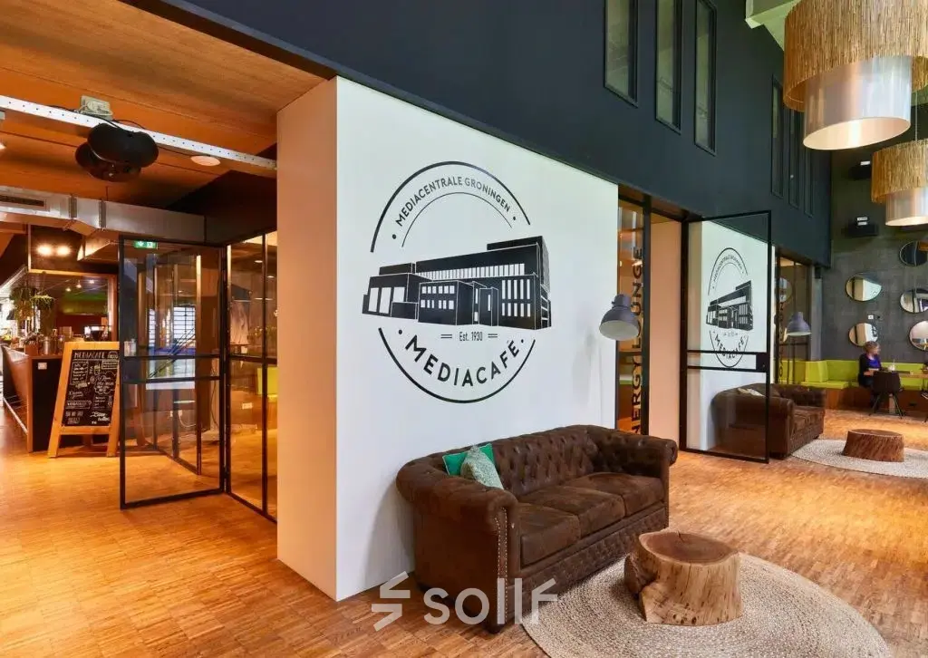Inviting office space at Helperpark 270-298, Groningen featuring a cozy lounge with plush seating and stylish decor, ideal for meetings in this office space rental. Natural light illuminates the room through large windows.