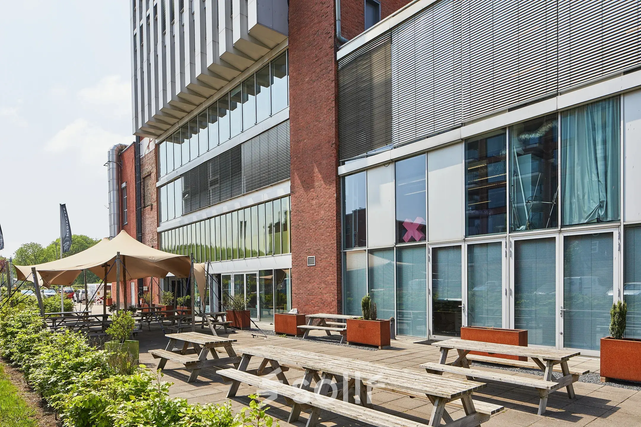 Exterior view of the office at Helperpark 270-298, Groningen, featuring wooden picnic tables outside a modern building. Ideal for businesses seeking office space rental in a contemporary setting.