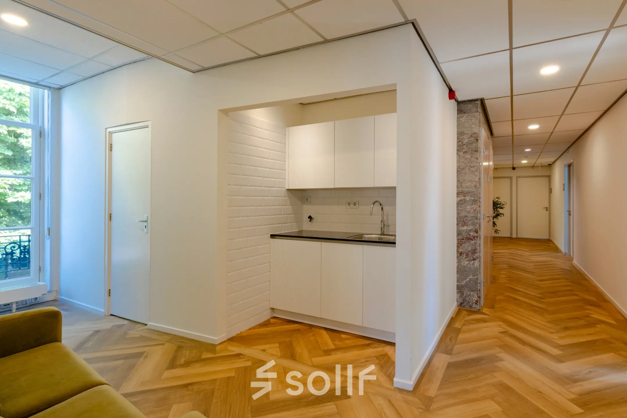 Office interior with stylish wooden flooring, a small kitchenette, and bright hallway at Kennemerplein 20, ideal for office space rental.