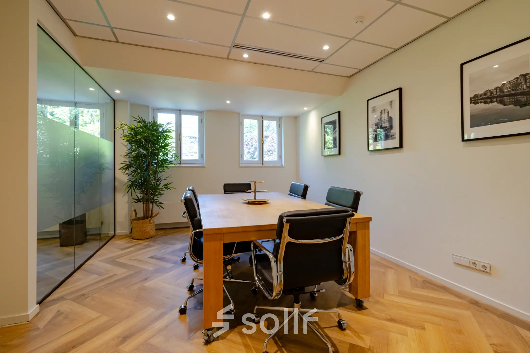 Modern conference room with a wooden table, black chairs, and wall art at Kennemerplein 20, Haarlem Centraal Station, ideal for office space rental.