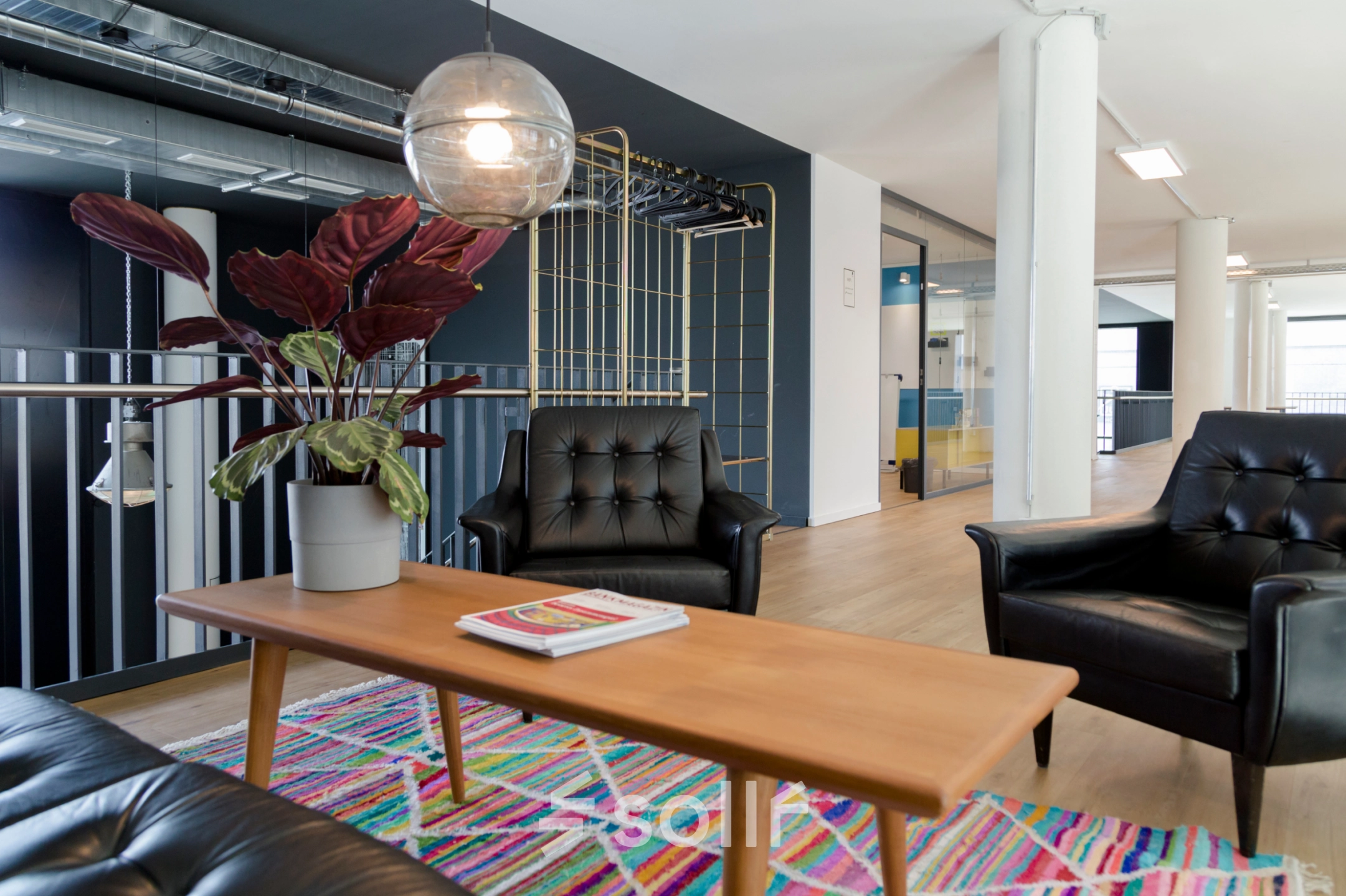 Furnished office space for rent at Versmannstraße 4, Hamburg Hafencity, featuring stylish black seating, a wooden coffee table, and a colorful rug under a modern light fixture.