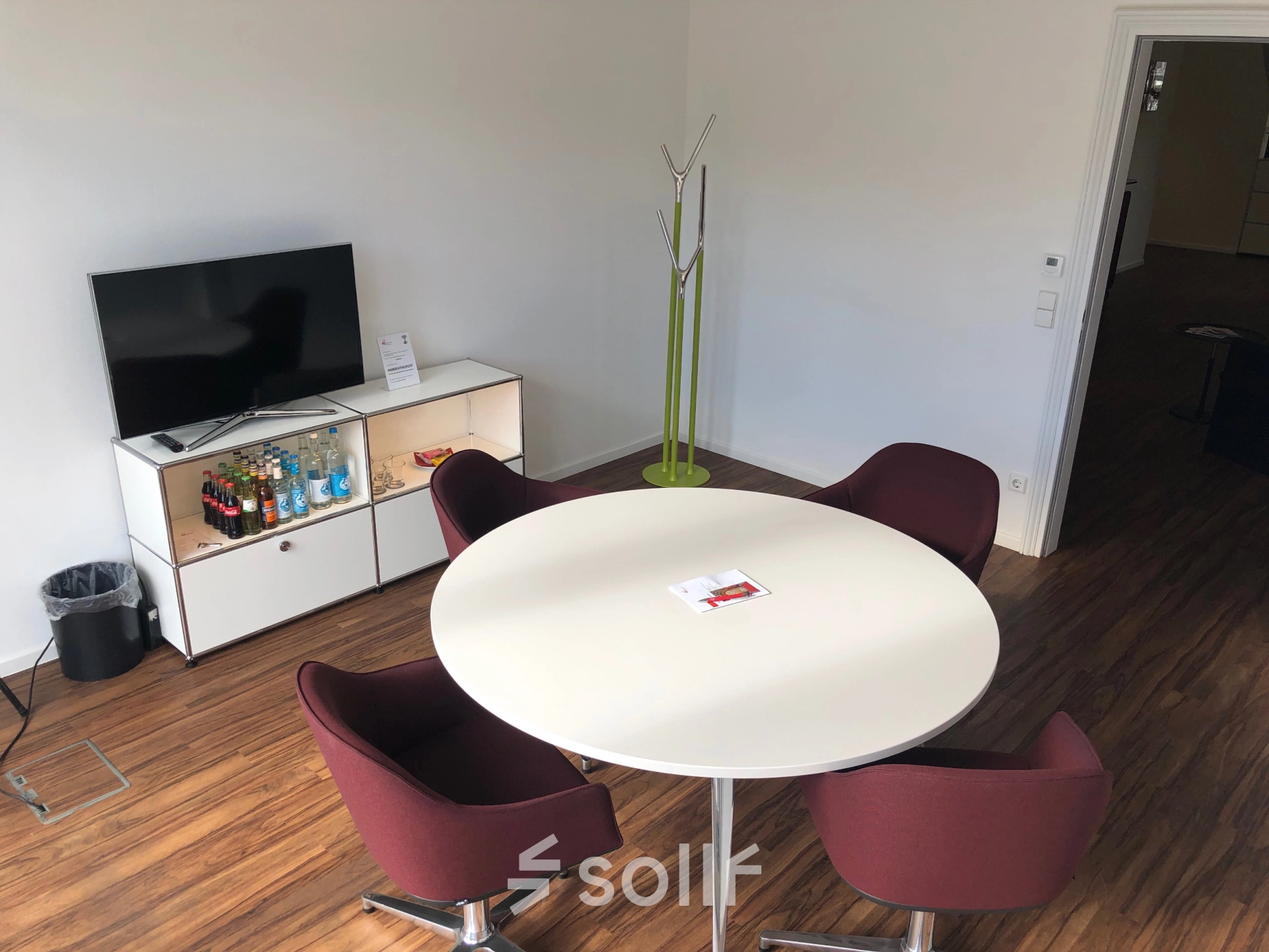 Cozy office space in Hamburg Neustadt with modern furnishings, including a round table and chairs, TV, and a small beverage shelf. Ideal for office space rental.