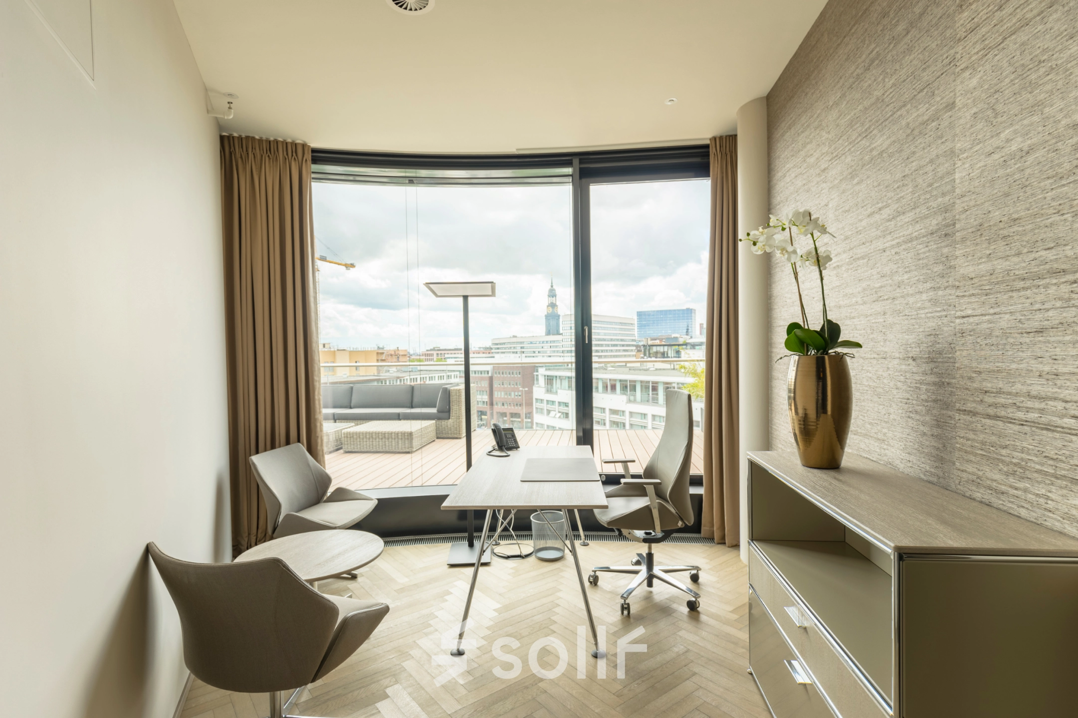Bright office space rental in Hamburg Neustadt with modern furnishings, featuring a desk, chairs, and a view of the cityscape through large windows.