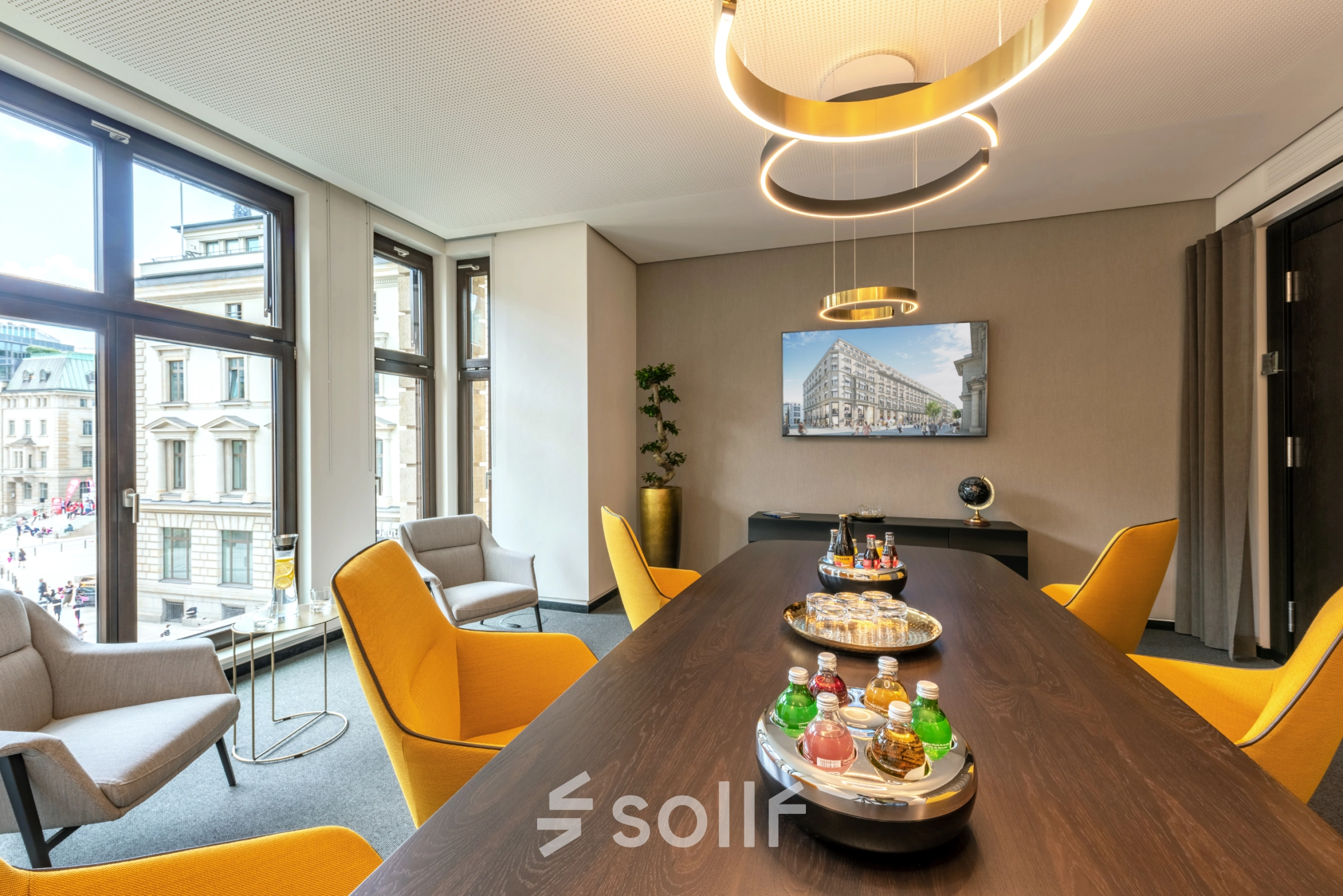 Bright office space on Alter Wall 32, Hamburg Old Town, featuring a large table, colorful chairs, and a city view. Ideal office space rental for meetings.