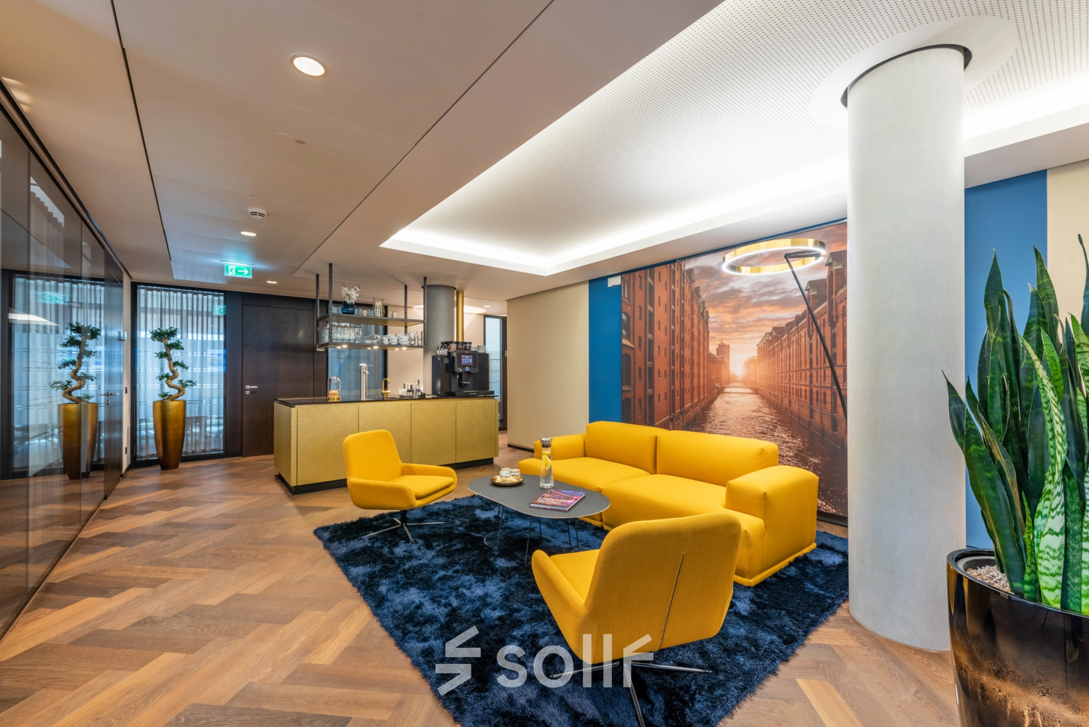 Welcoming lounge area at Alter Wall 32, Hamburg Old Town, featuring modern yellow seating, a blue rug, and a large cityscape mural, ideal for office space rental.