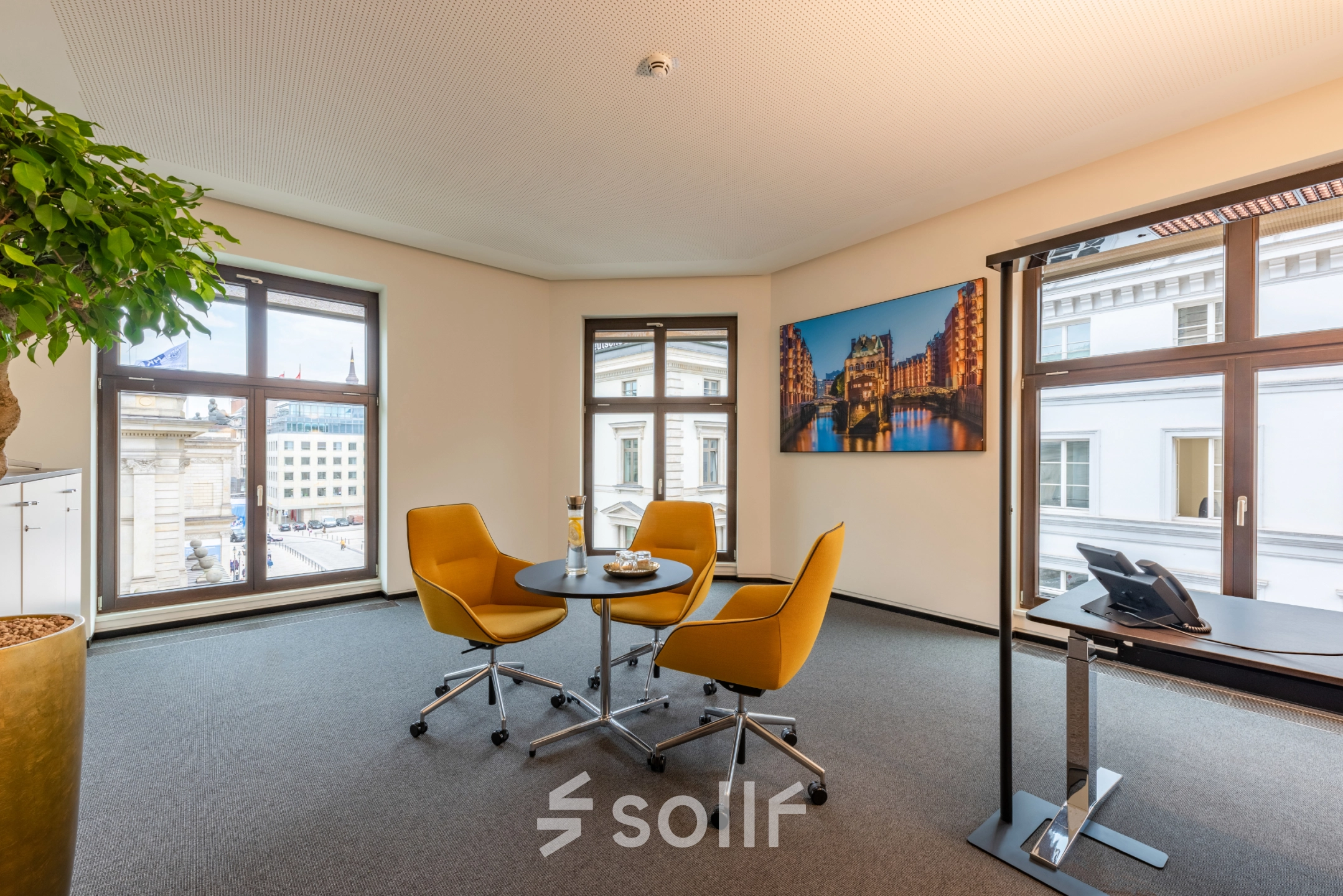 Well-lit office to rent at Alter Wall 32, Hamburg Old Town, featuring a small meeting area with chairs and desk, ideal for business discussions.