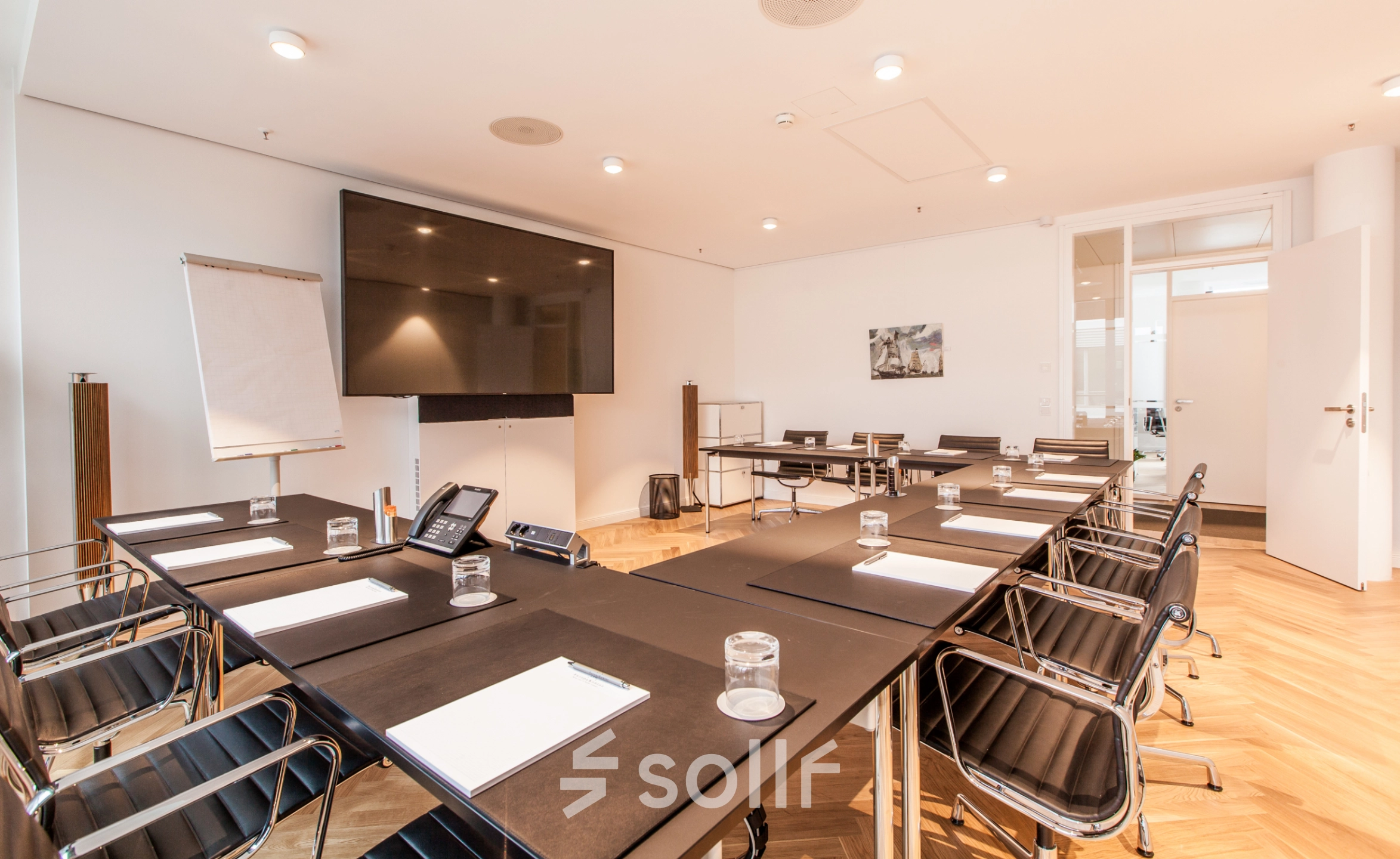 Spacious conference room at Ballindamm 39, Hamburg Old Town, ideal for office space rental. Features sleek tables, chairs, and a large screen for presentations.
