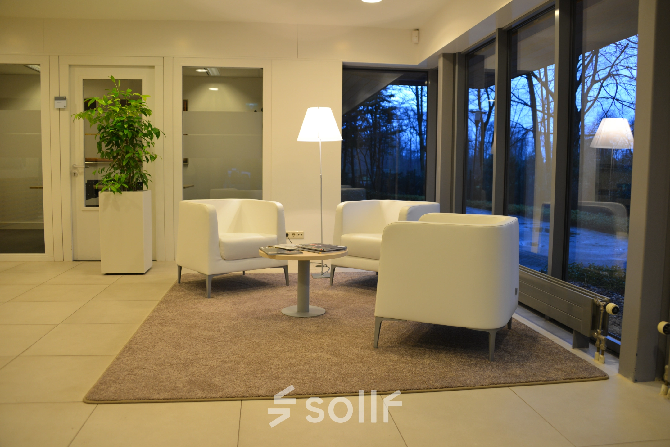 Modern office space at Herenweg 115, Heemstede, featuring a cozy seating area with white chairs and a lamp, ideal for office space rental.