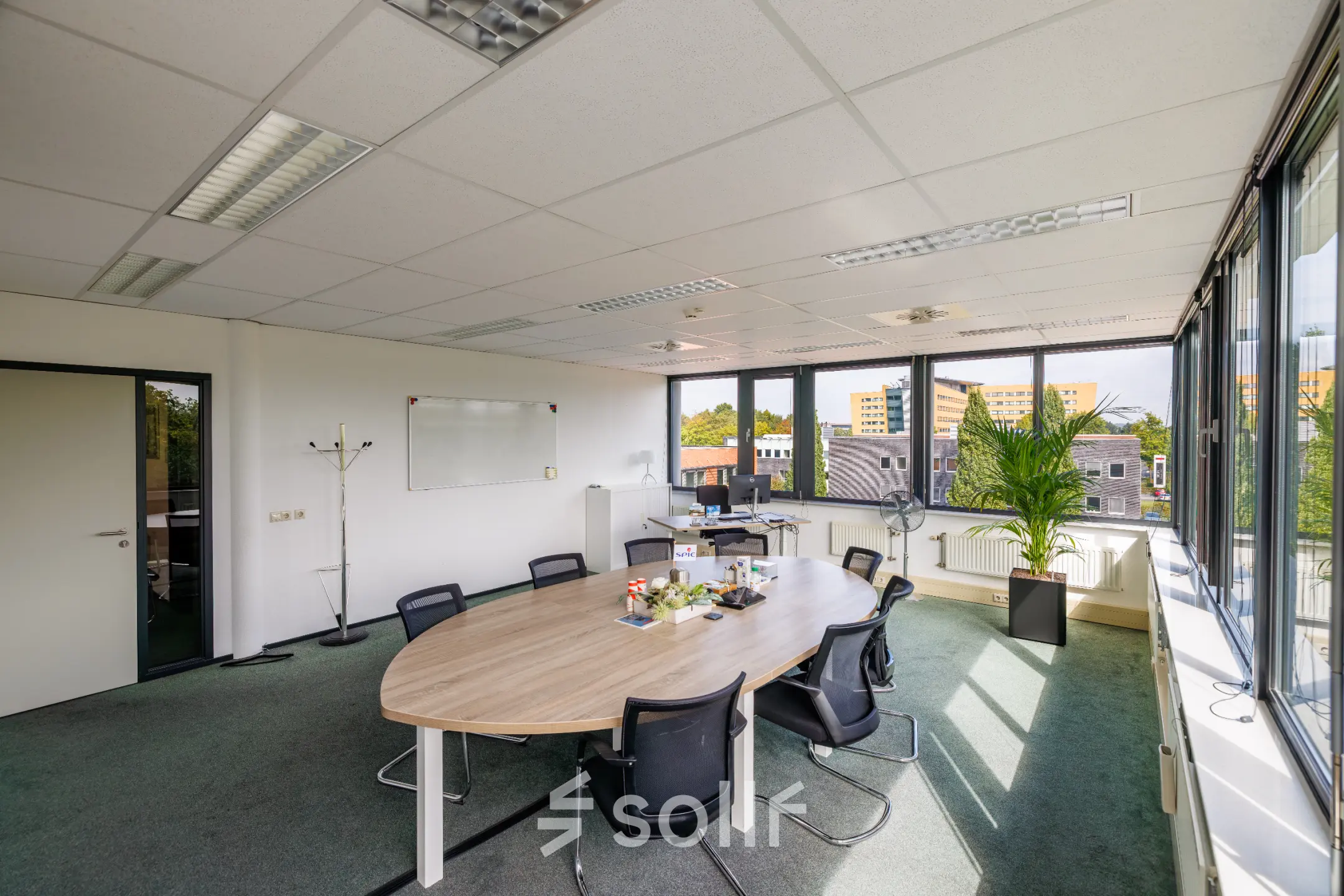 Bright office space for rent at Welbergweg 60, Hengelo, featuring a large oval table with chairs, whiteboard, and window views, ideal for meetings or collaborative work.