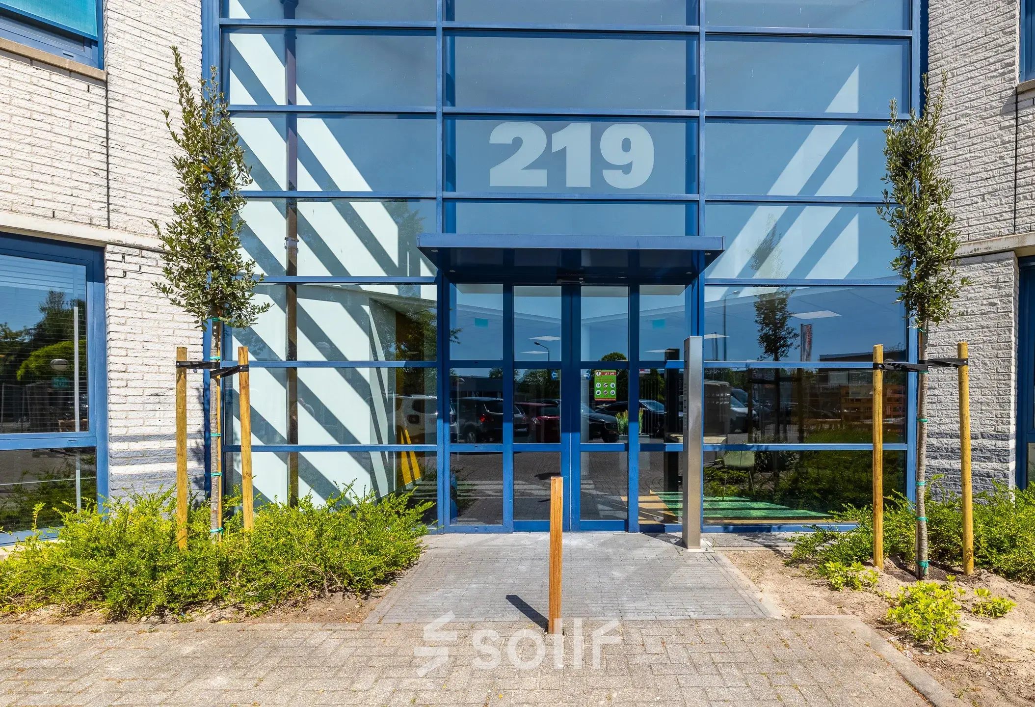 Entrance of an office building at Franciscusweg 219, Hilversum, showcasing modern glass architecture with visible office space rental opportunities.