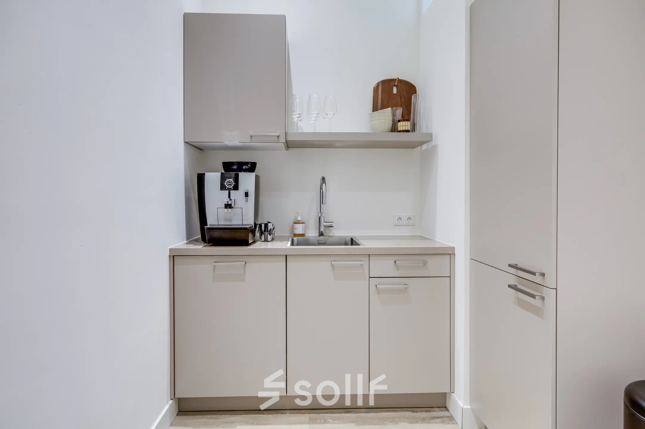 Compact kitchen area in an office space, featuring a coffee machine and storage cabinets. Ideal for office space rental opportunities.