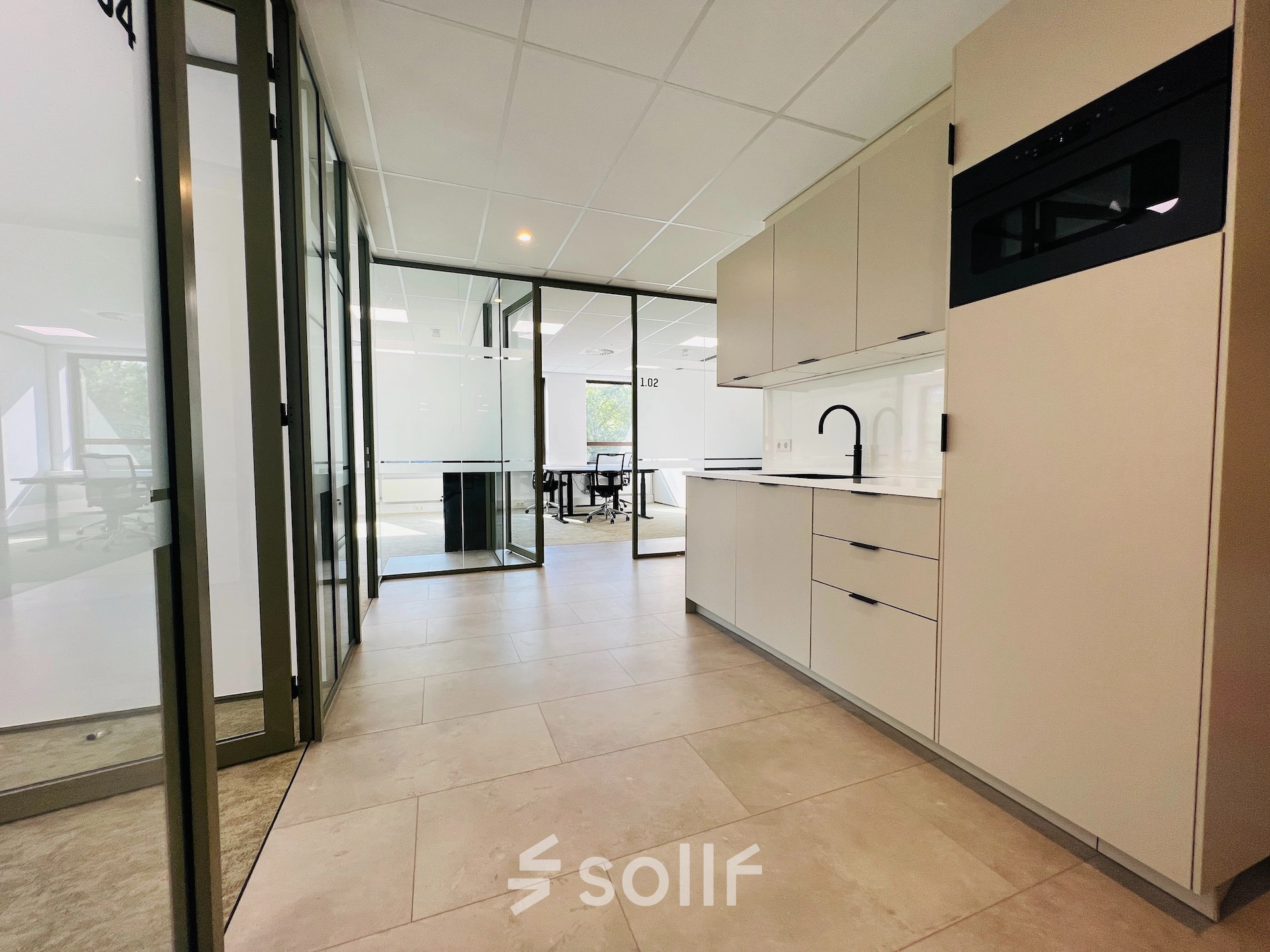 Modern office space available for rent in Hilversum's Marathon 2, featuring a sleek kitchenette beside spacious workspaces.