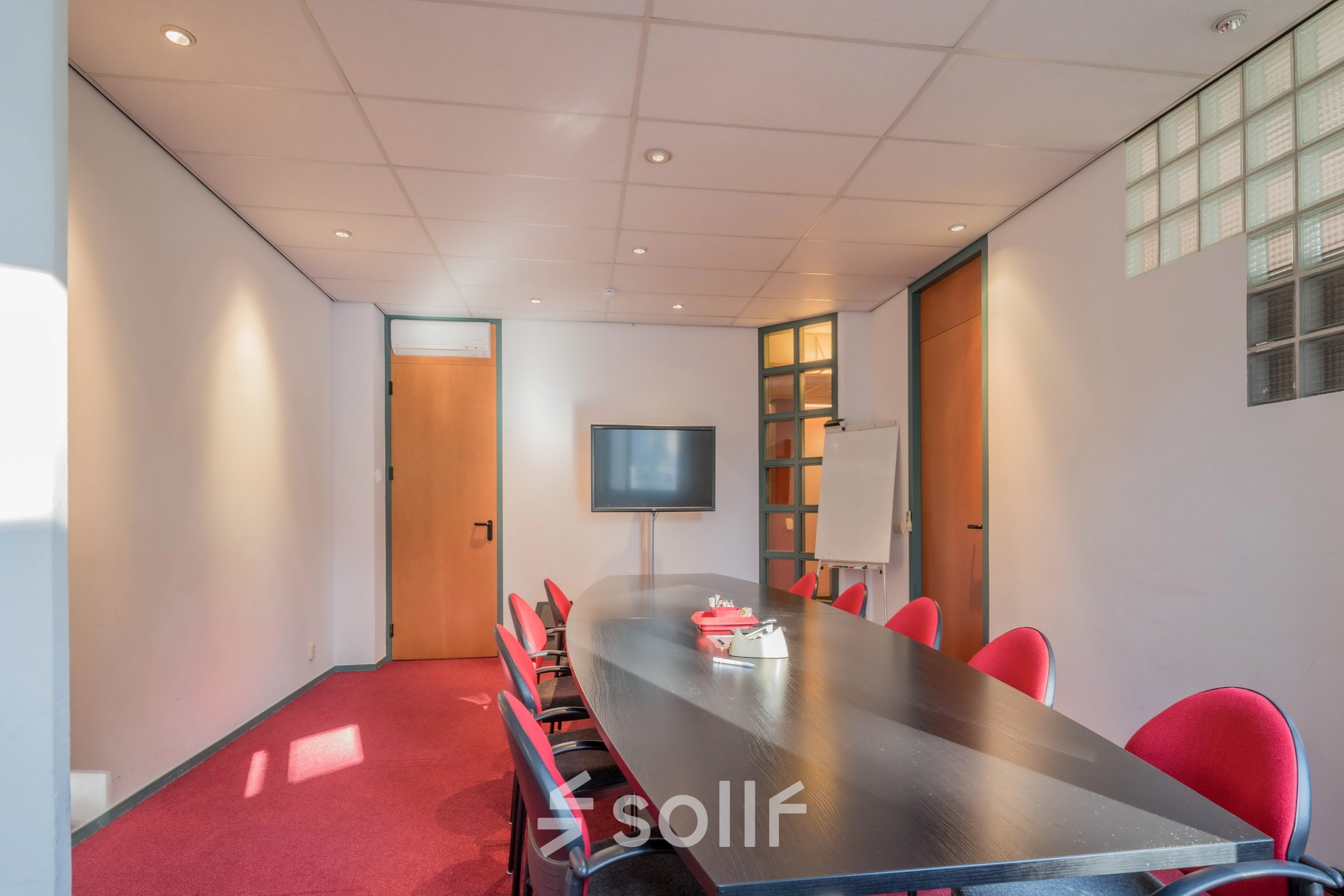 Office space for rent at Mozartlaan 27, Hilversum, featuring a conference room with a long table, red chairs, a TV, and a whiteboard.