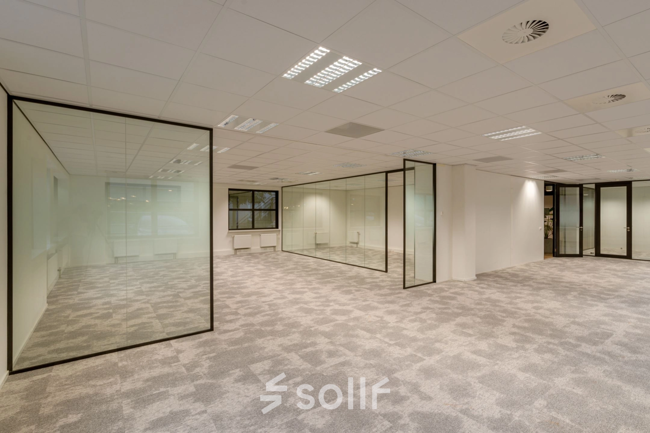 Spacious, unfurnished office for rent at Olympia 1, Hilversum featuring glass partitions and a carpeted floor.