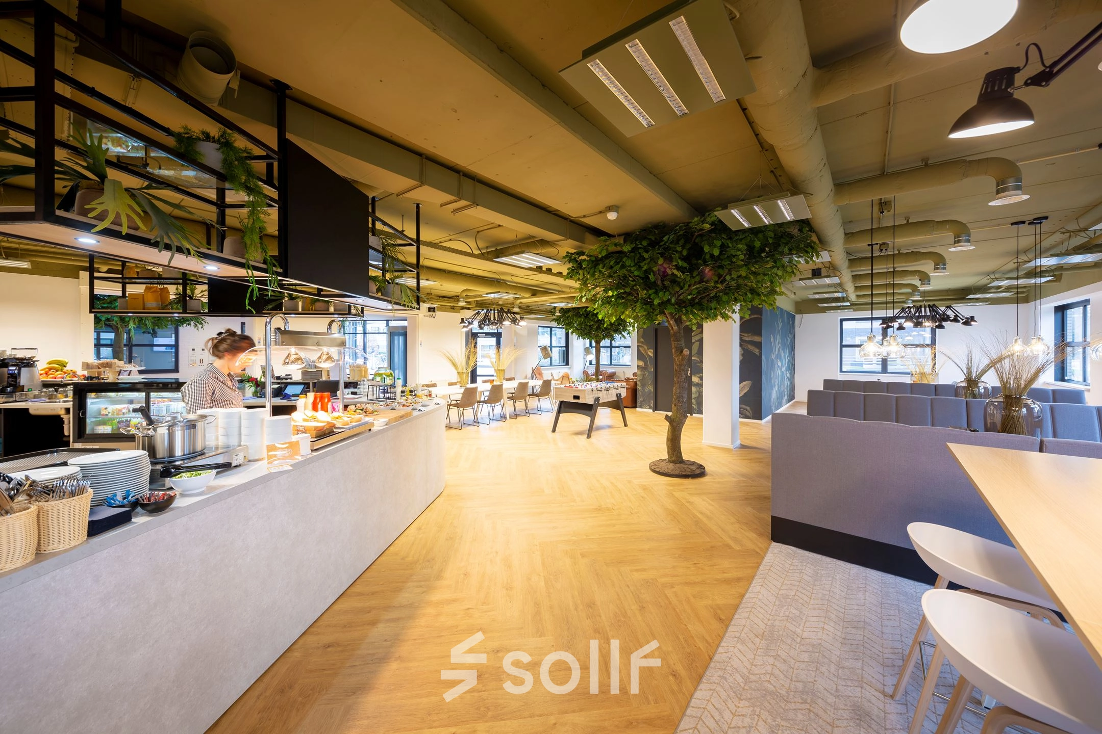 Spacious and modern workspace at Olympia 1, Hilversum, featuring a cafeteria area with a person serving refreshments and stylish furnishings perfect for office space rental.