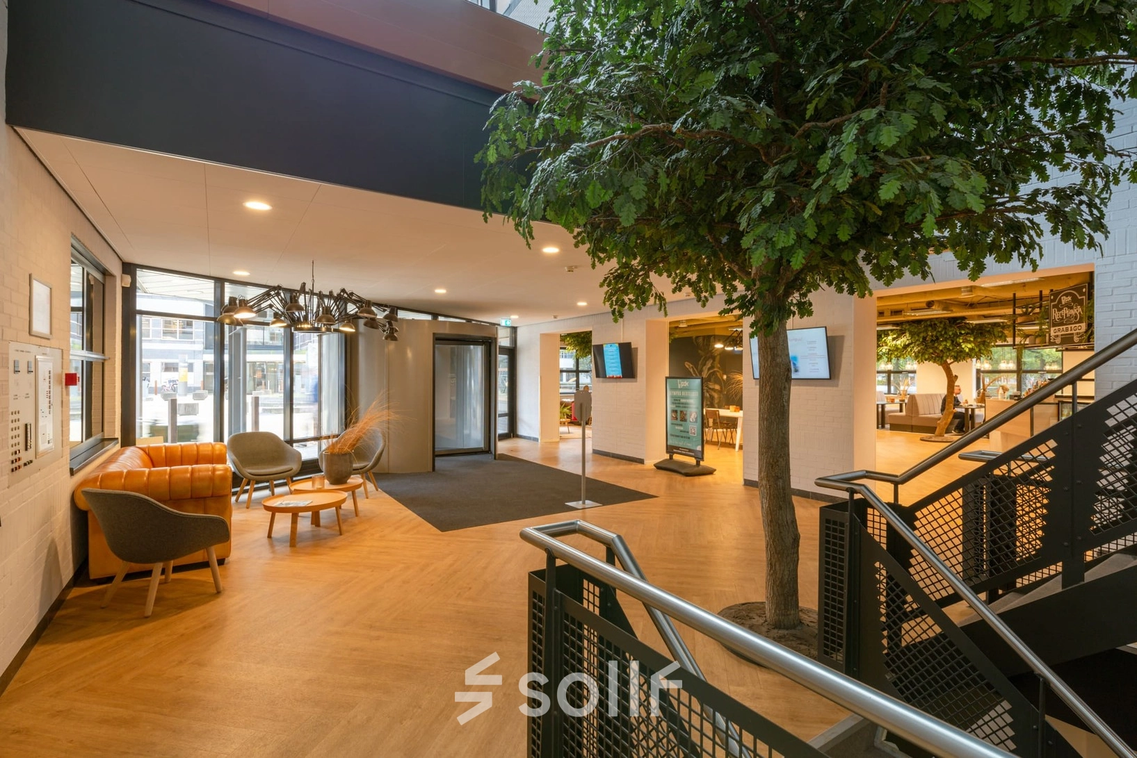 Spacious office reception with modern seating and a decorative tree at Olympia 1, Hilversum, ideal for office space rental.