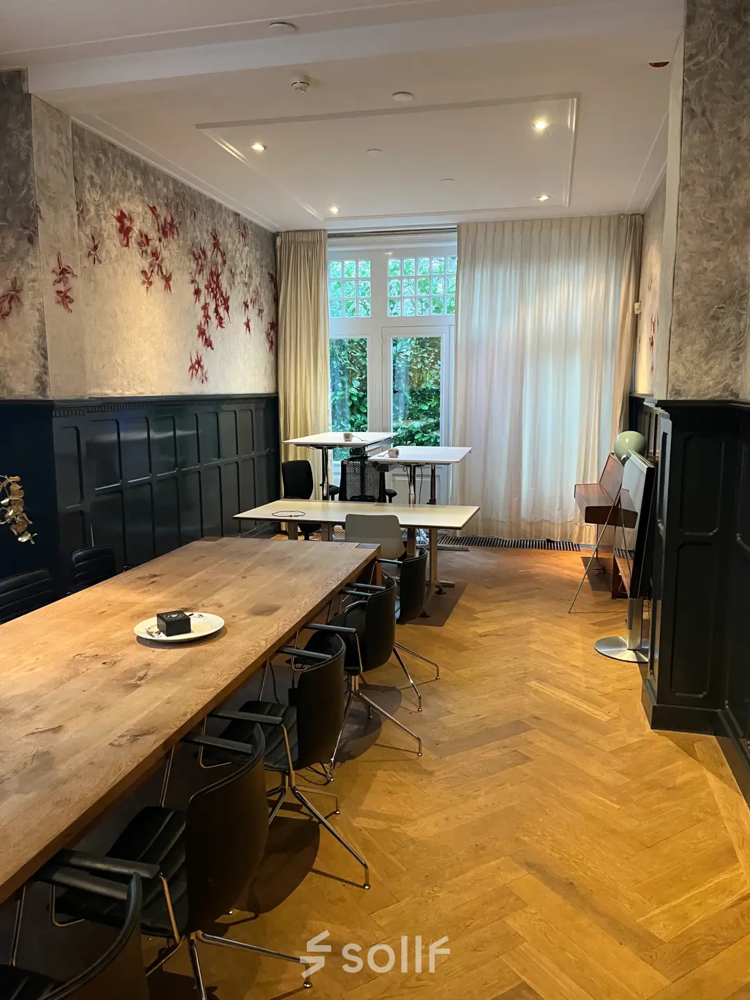 Interior view of a furnished office space for rent at Oude Enghweg 8, Hilversum, featuring wooden tables and black chairs under soft lighting.