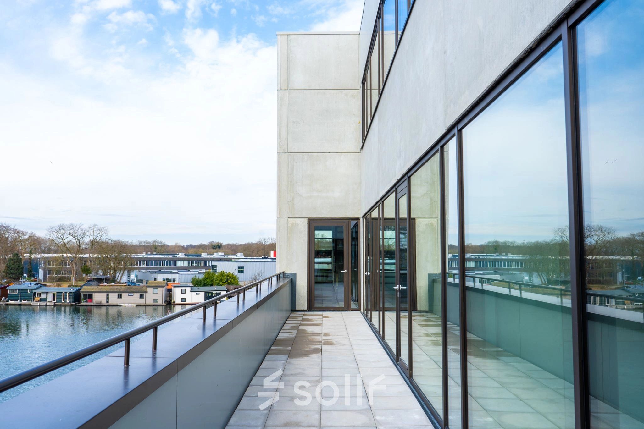 View of an office building's exterior at Zuiderloswal 55, Hilversum, highlighting large glass windows overlooking a waterfront. Ideal location for office space rental with modern architecture.
