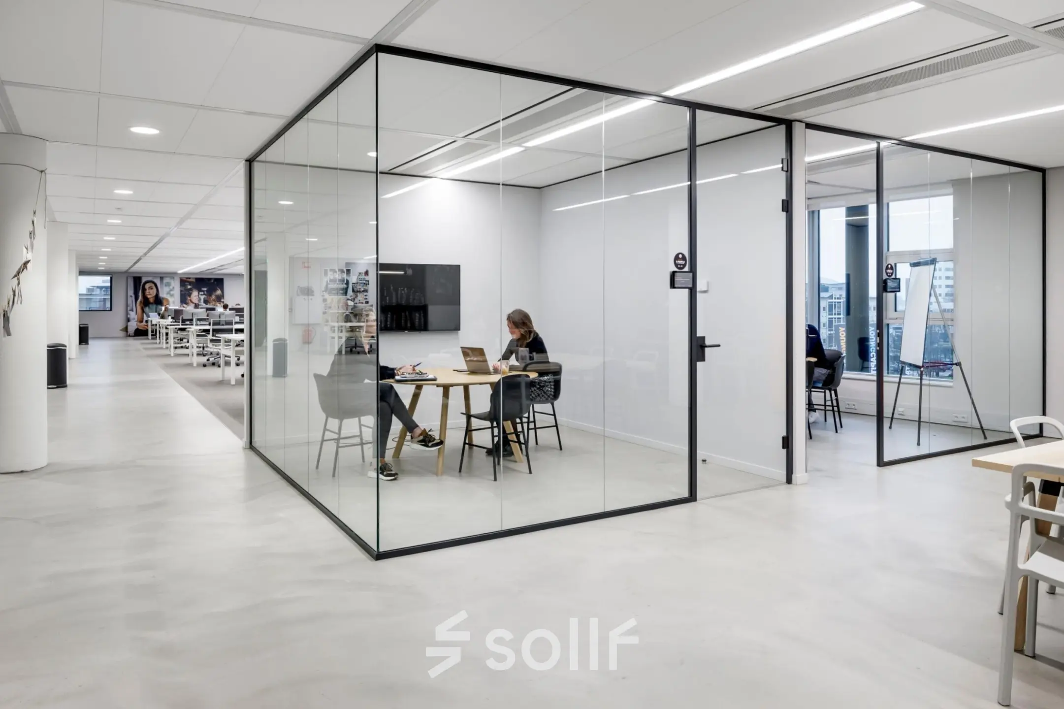 Modern office space at Siriusdreef 16, Hoofddorp featuring glass-walled meeting rooms with people engaged in work activities. Ideal for those seeking office space rental.