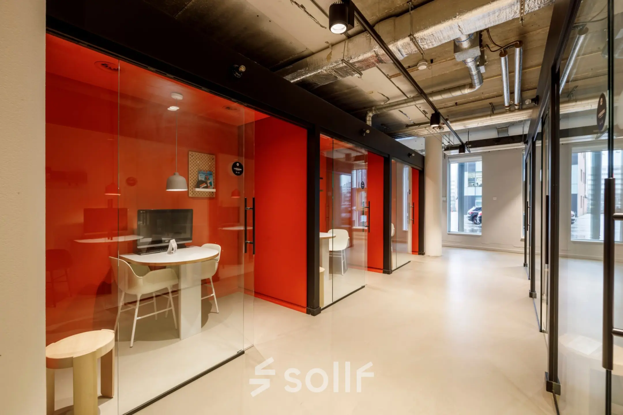 Modern office space rental at Siriusdreef 16, Hoofddorp, featuring a corridor with vibrant red glass enclosed meeting rooms and stylish lighting.