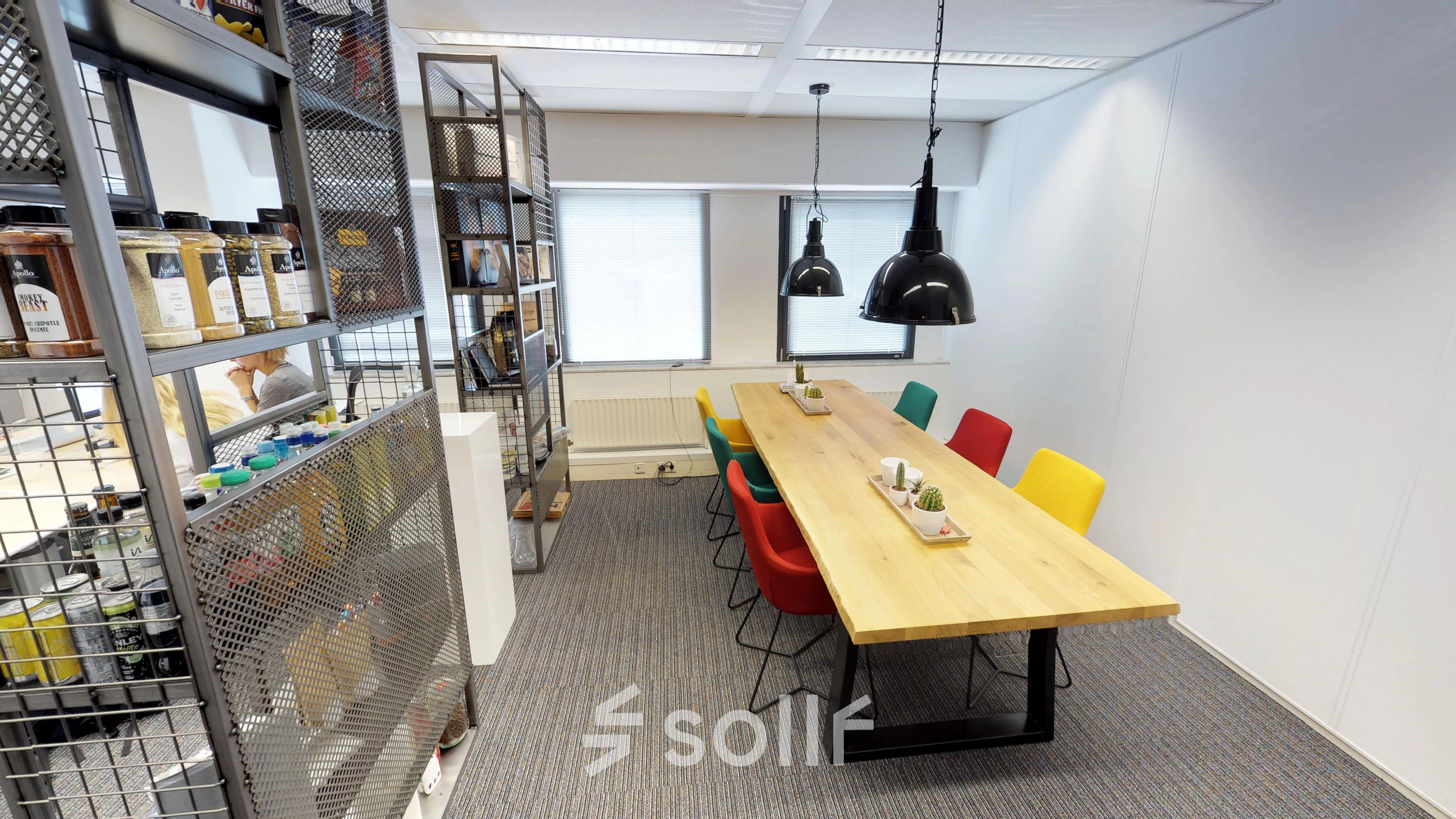 Bright office space at Meidoornkade 22, Houten, featuring a long wooden table with colorful chairs, ideal for meetings. Shelves line one wall, adding functional storage.