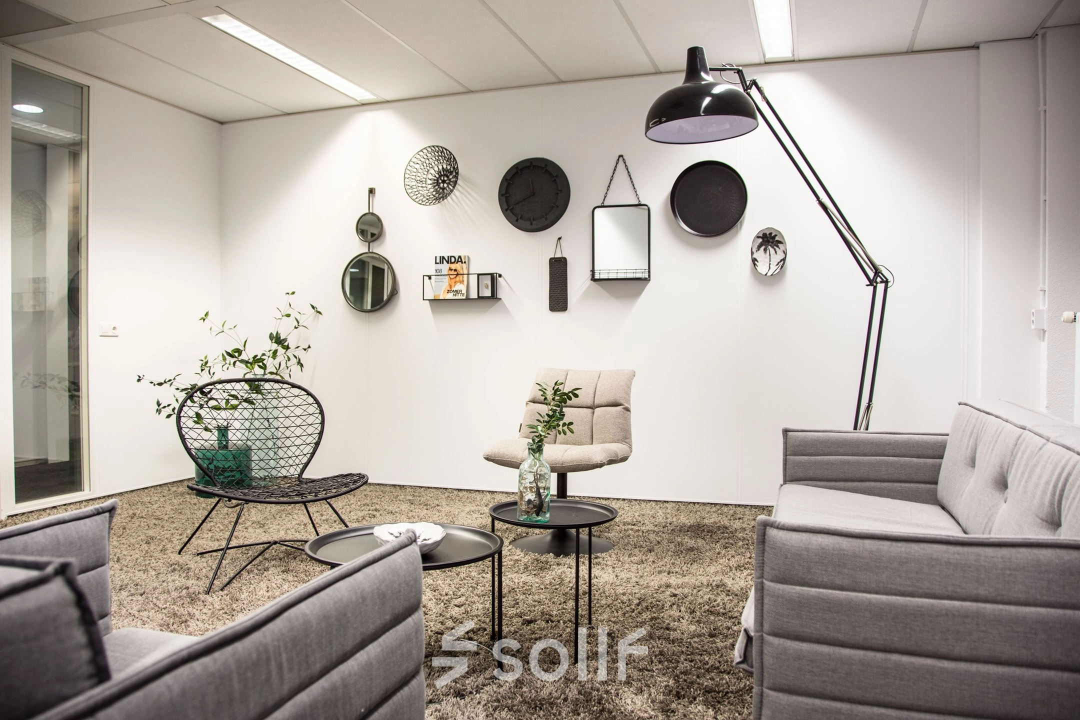 Furnished office space for rent featuring stylish gray sofas, a standing lamp, and decorative wall items, located at Meidoornkade 22, Houten.