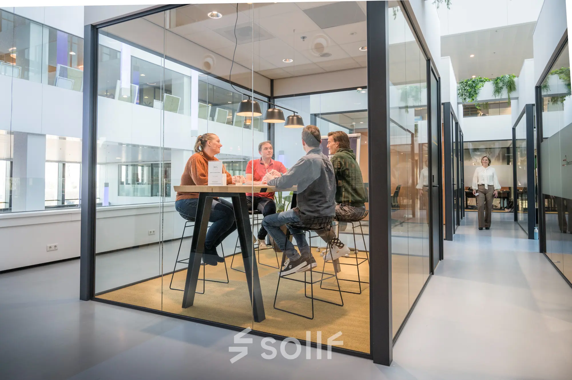 Modern office space rental at Bargelaan 200, Leiden, featuring a glass-enclosed meeting area with people engaged in discussion around a high table.