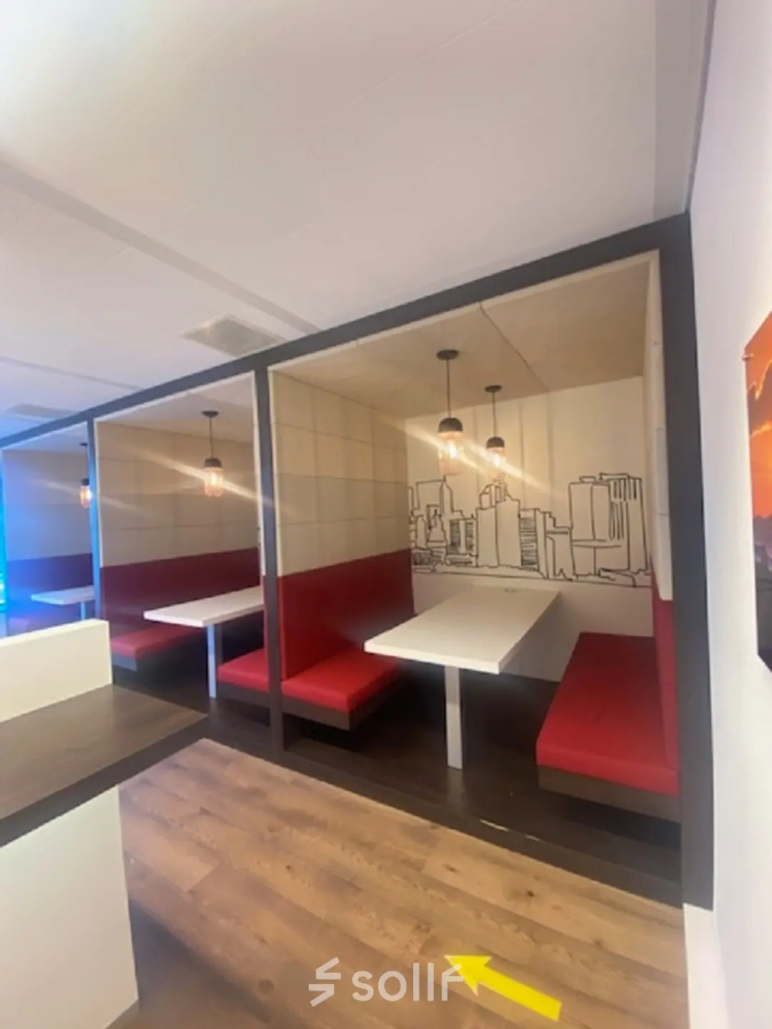 Furnished office space for rent at Mendelweg 30 in Leiden, featuring cozy booths with red seating and cityscape artwork.