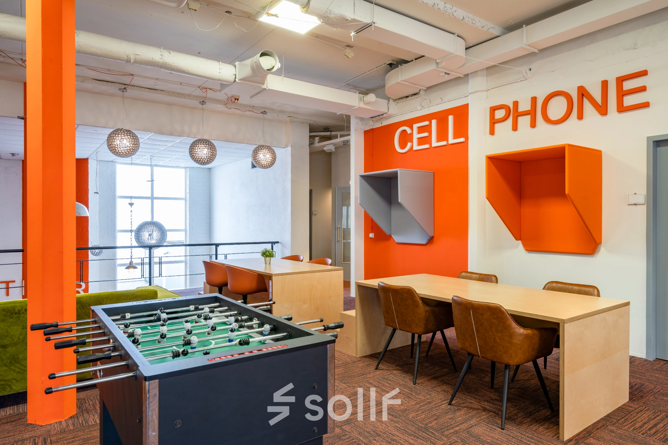 Modern interior office space at Touwbaan 38, Leiderdorp, featuring a vibrant lounge area with a foosball table, seating, and phone booths. Available for office space rental in a lively setting.