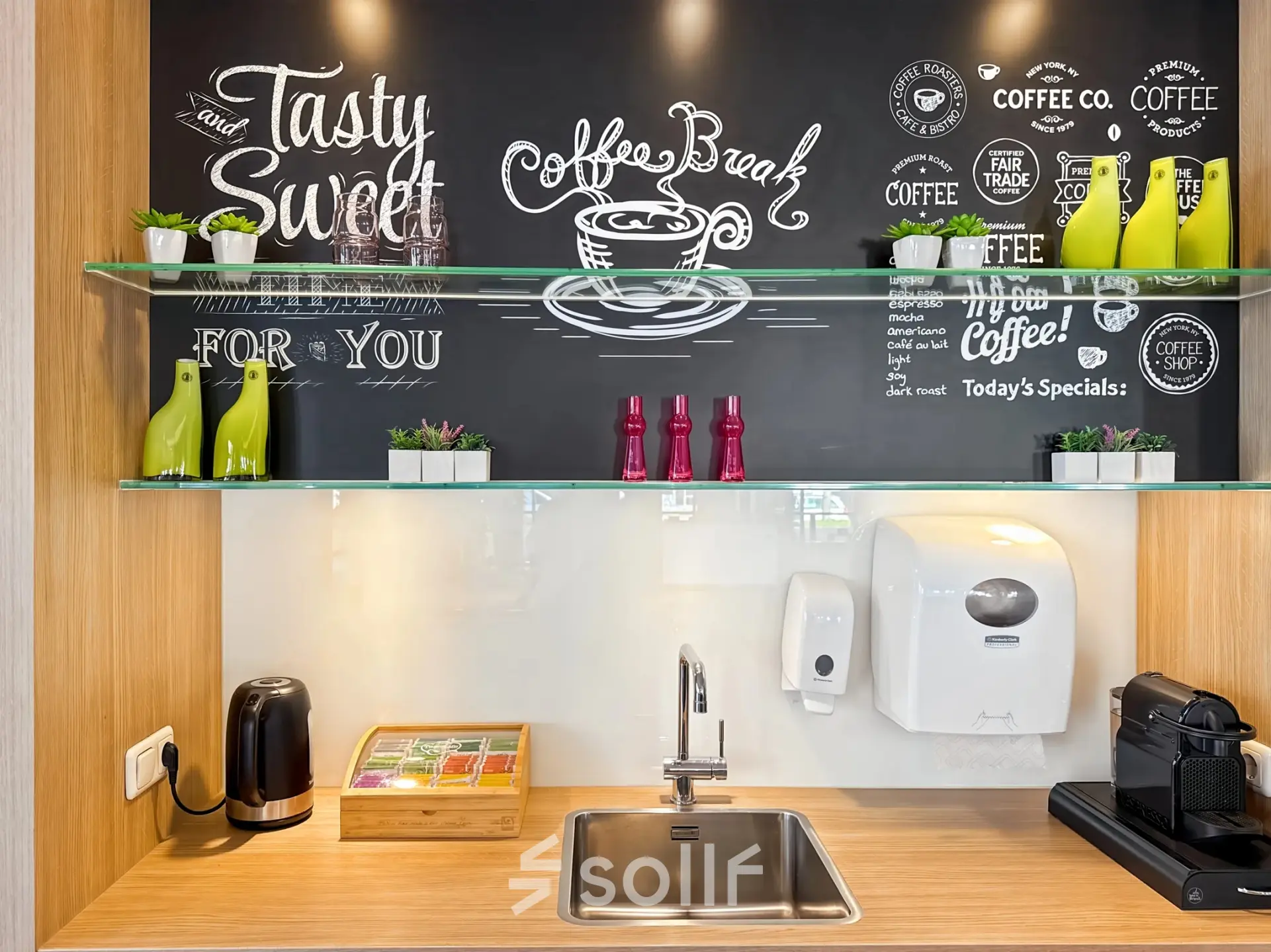 A stylish pantry area in an office to rent at Robert Schumandomein 2, Maastricht, featuring a sink, coffee machine, and decorative chalkboard walls with vibrant accents.