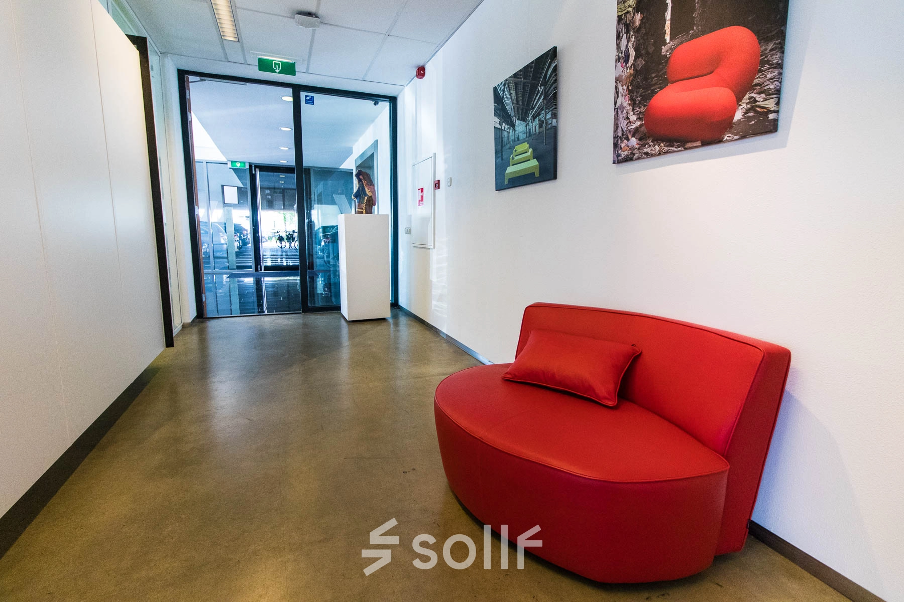 Spacious office entrance at Brieltjenspolder 28, Made, featuring a vibrant red couch and art on the walls, ideal for office space rental.