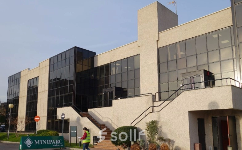 Modern office building at Calle de la Azalea 1, Madrid Alcobendas, featuring large glass windows ideal for office space rental. Individuals are seen walking outside, highlighting an office to rent.