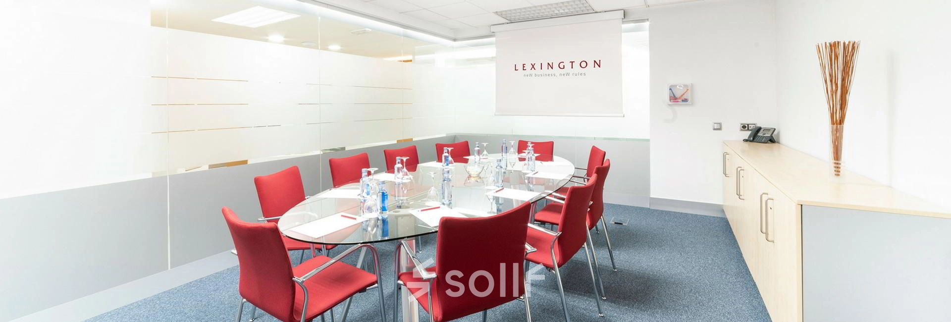 Bright modern conference room with red chairs and a glass table set for a meeting, ideal for office space rental in Madrid Alcobendas.