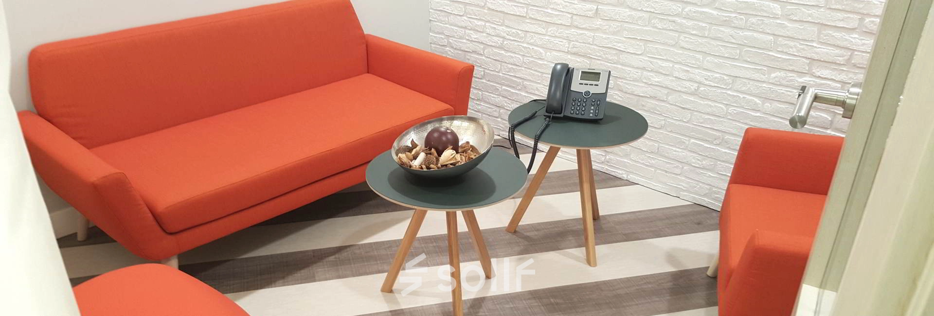 Cozy office space in Madrid Azca with vibrant orange seating and modern décor, ideal for small meetings or informal discussions.