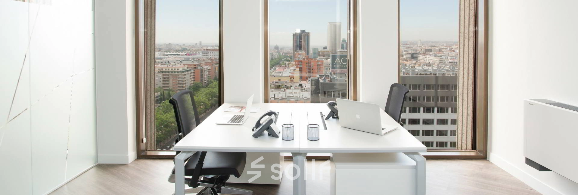 Bright office space with two desks, chairs, and a view of Madrid's skyline from Paseo de la Castellana 141. Perfect for rent office space seekers.