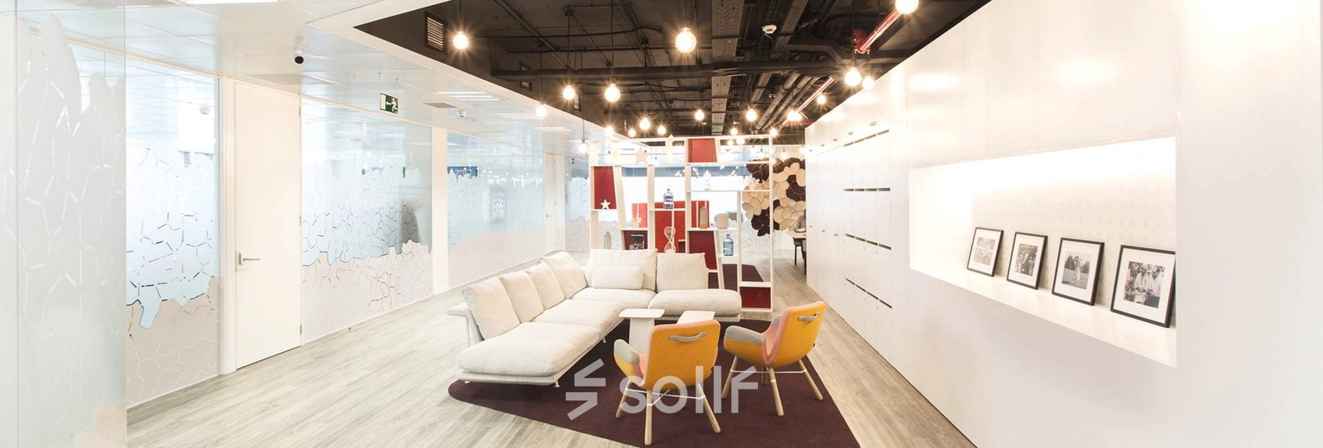 A spacious, modern office interior at Paseo de la Castellana 79, Madrid Azca, featuring contemporary furnishings including a comfortable sofa and stylish chairs under warm lighting.