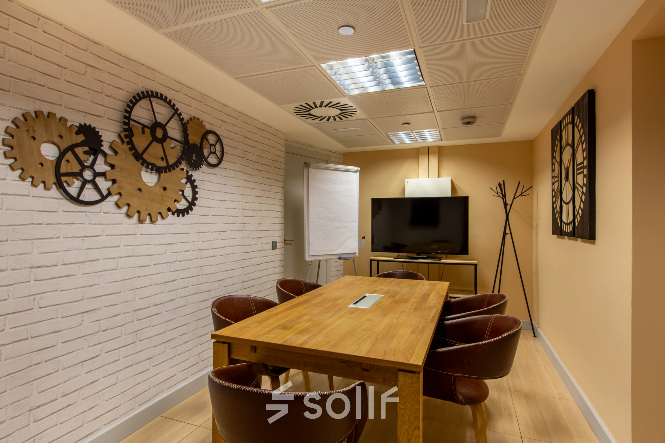 Interior of a furnished office space at Paseo de la Castellana 95 in Madrid Azca, featuring a table, chairs, and wall decor. A screen and flip chart suggest it's ideal for meetings.