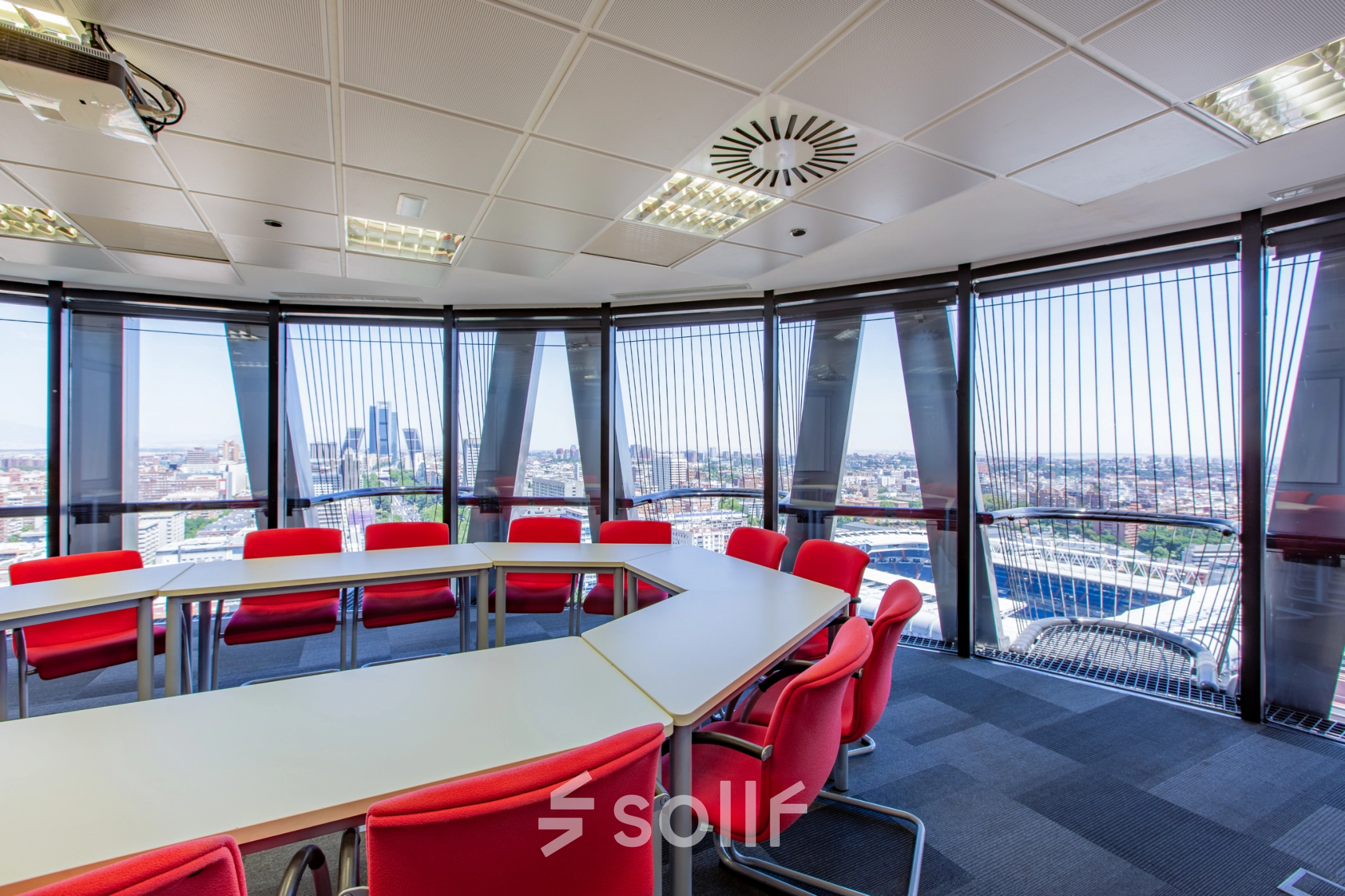 Bright office space for rent in Madrid Azca, featuring large windows with a stunning city view, and modern red and white furnishings arranged in a conference style.