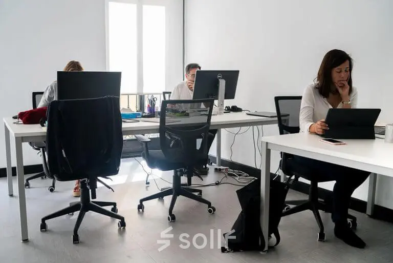 Professionals working at desks in a well-lit office at calle de las Huertas 11, ideal for office space rental in Madrid Center.