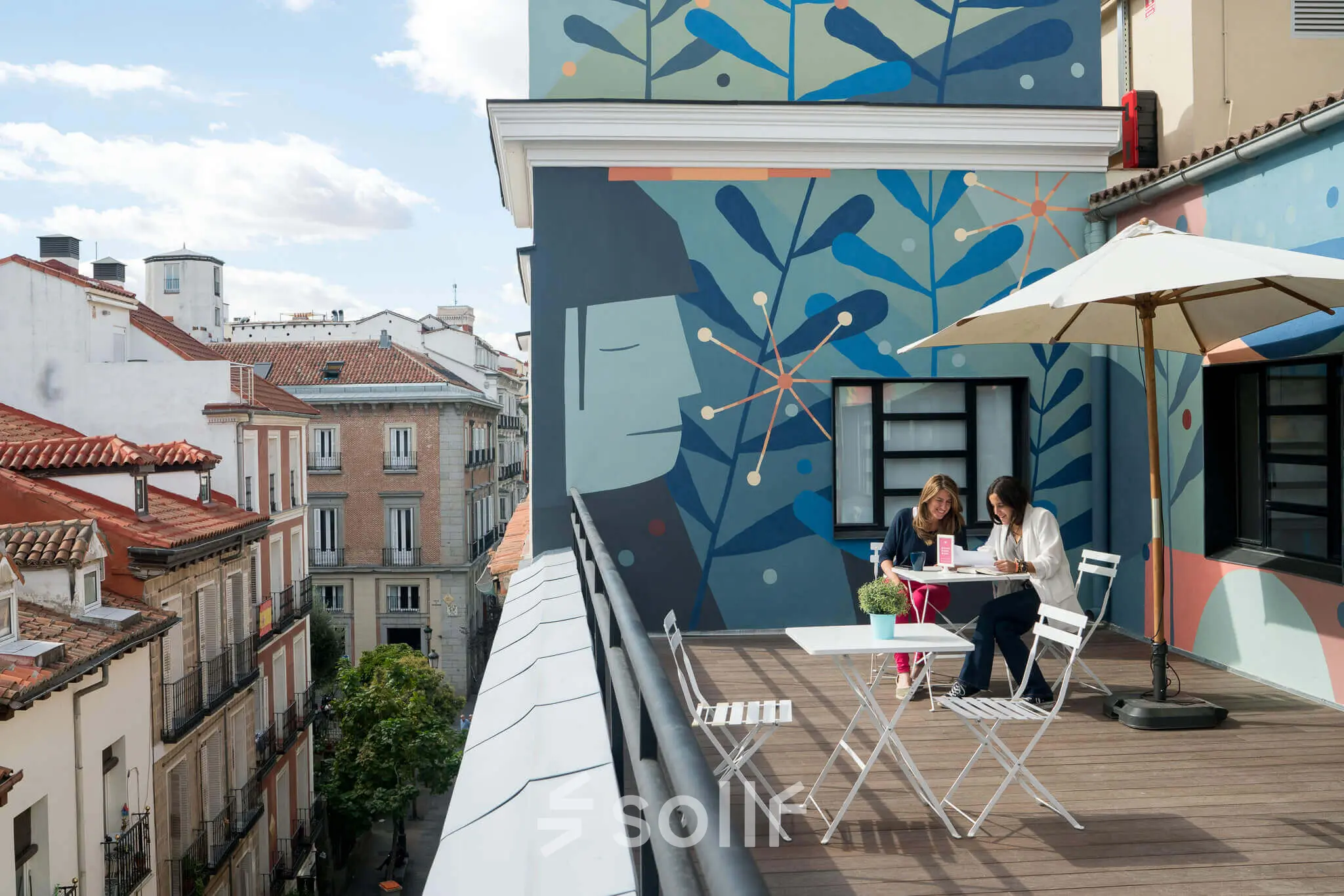 Terrace at calle de las Huertas 11, Madrid Center, with two people collaborating at a table, surrounded by colorful murals. Ideal spot for rent office space discussions.