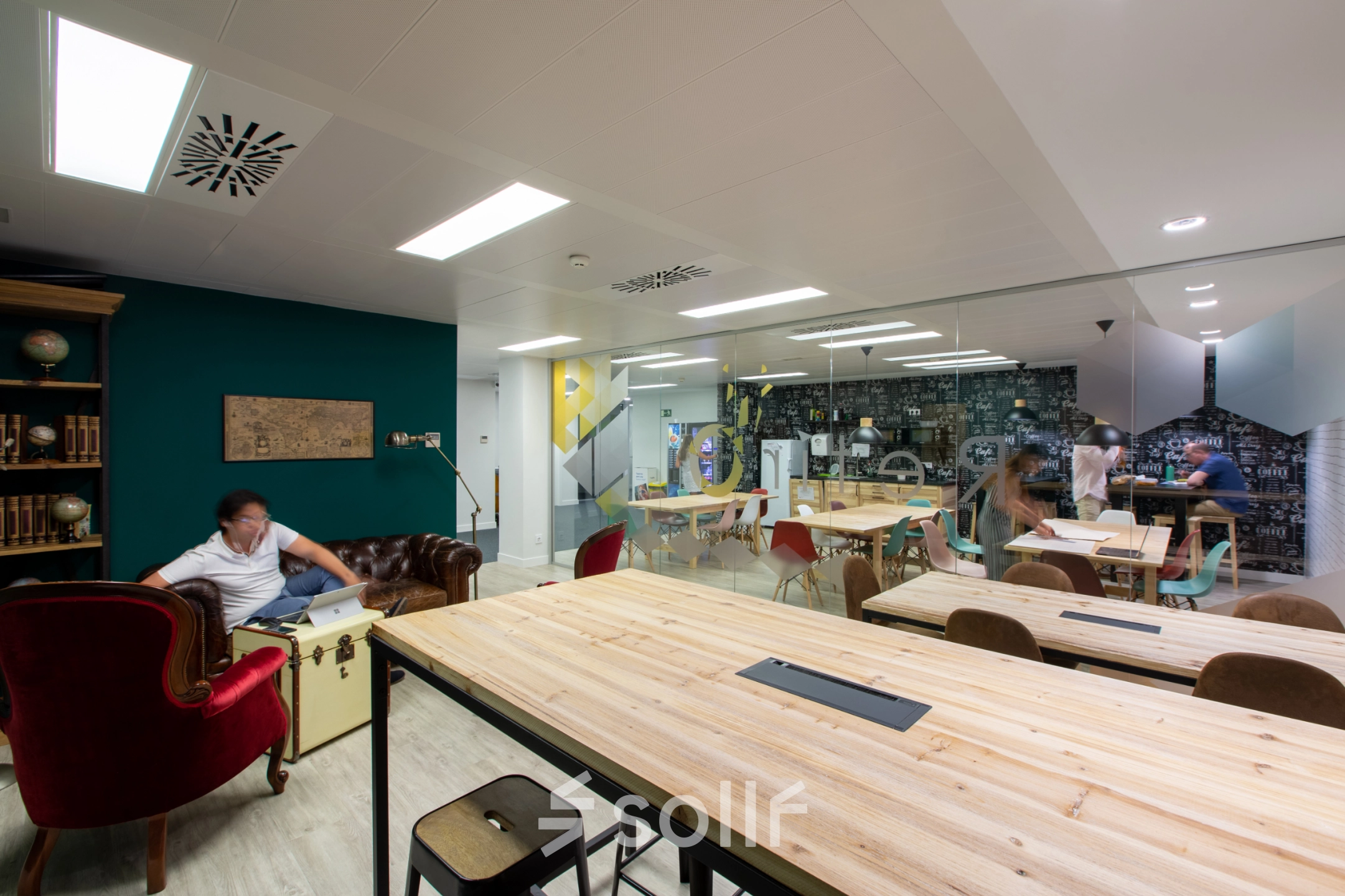 Shared office space to rent in Madrid Retiro, featuring long wooden tables, eclectic seating, and people collaborating in a vibrant setting. Ideal for office space rental.
