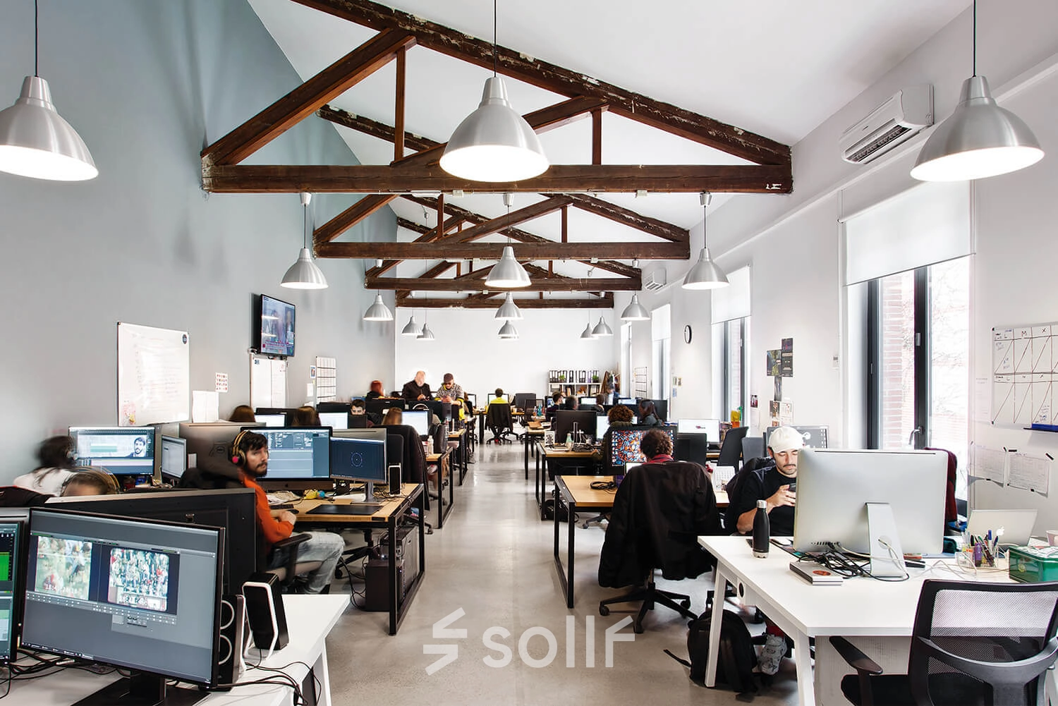 Modern office space in Madrid Retiro at Calle Vandergoten 1 with professionals working at computers under exposed wooden beams, ideal for office space rental.