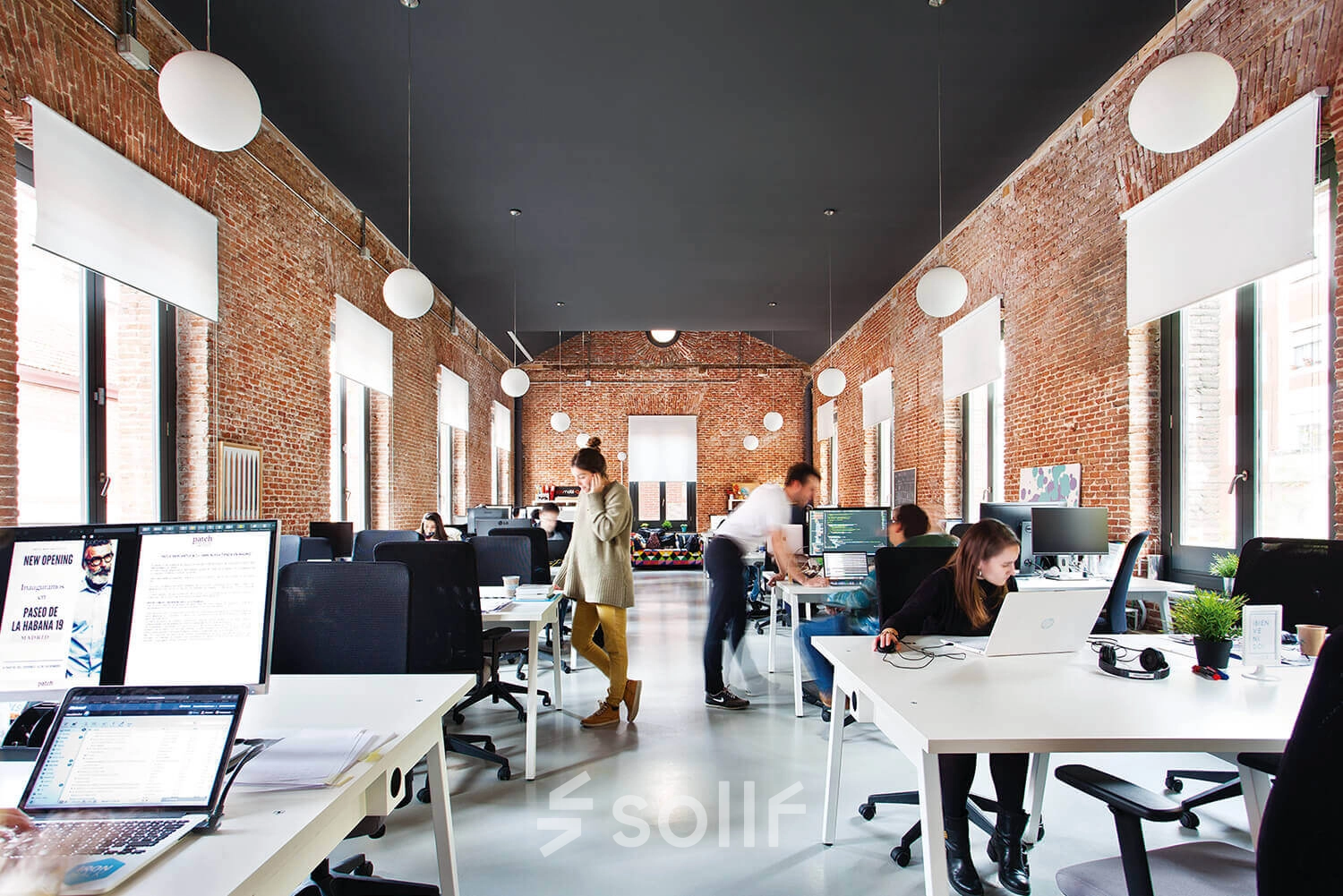 Spacious office to rent on Calle Vandergoten 1, Madrid Retiro, showcasing an open, brick-walled workspace with individuals actively working at desks.