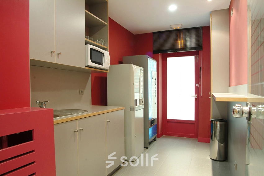 Compact office pantry with red walls, equipped with a microwave, mini fridge, and vending machine for efficient office space rental.