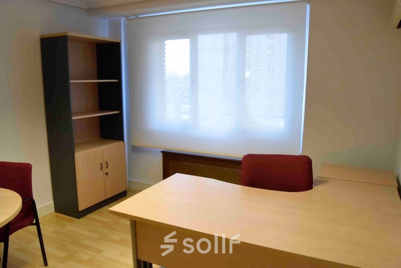 Bright office space with wooden desks and an empty bookshelf at Calle Capitan Haya 60, ideal for office space rental in Madrid Tetuán.