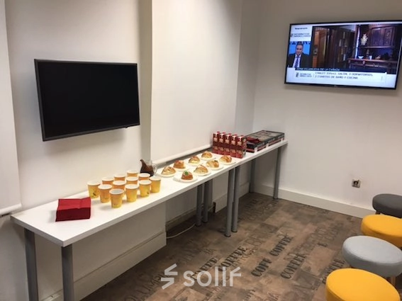 Cozy office lounge with a long table set for snacks, beverages, and a wall-mounted TV. Ideal for office space rental in Calle Capitan Haya 60, Madrid Tetuán.